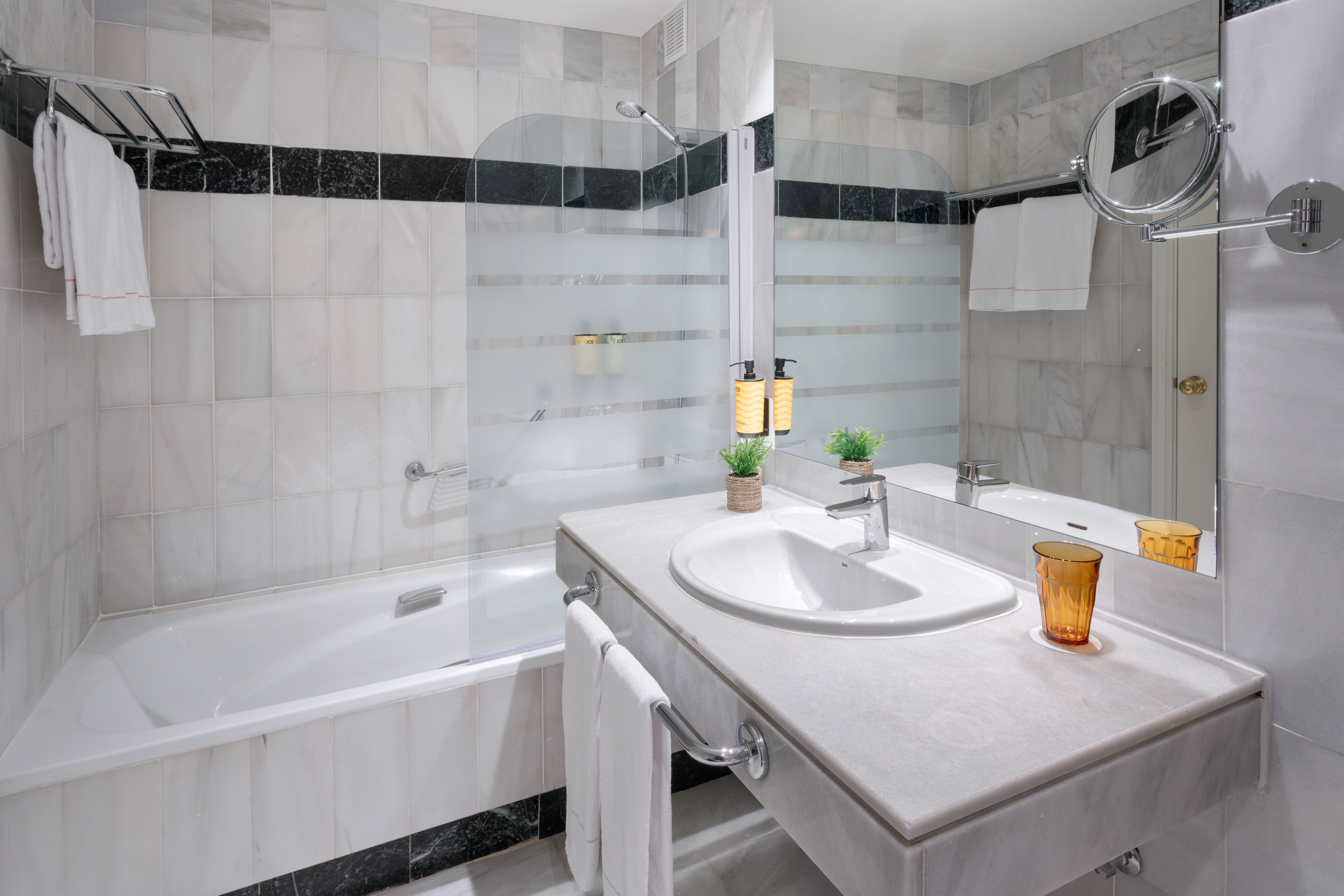 Baño moderno de hotel con bañera, lavabo de mármol, ducha y toallas.