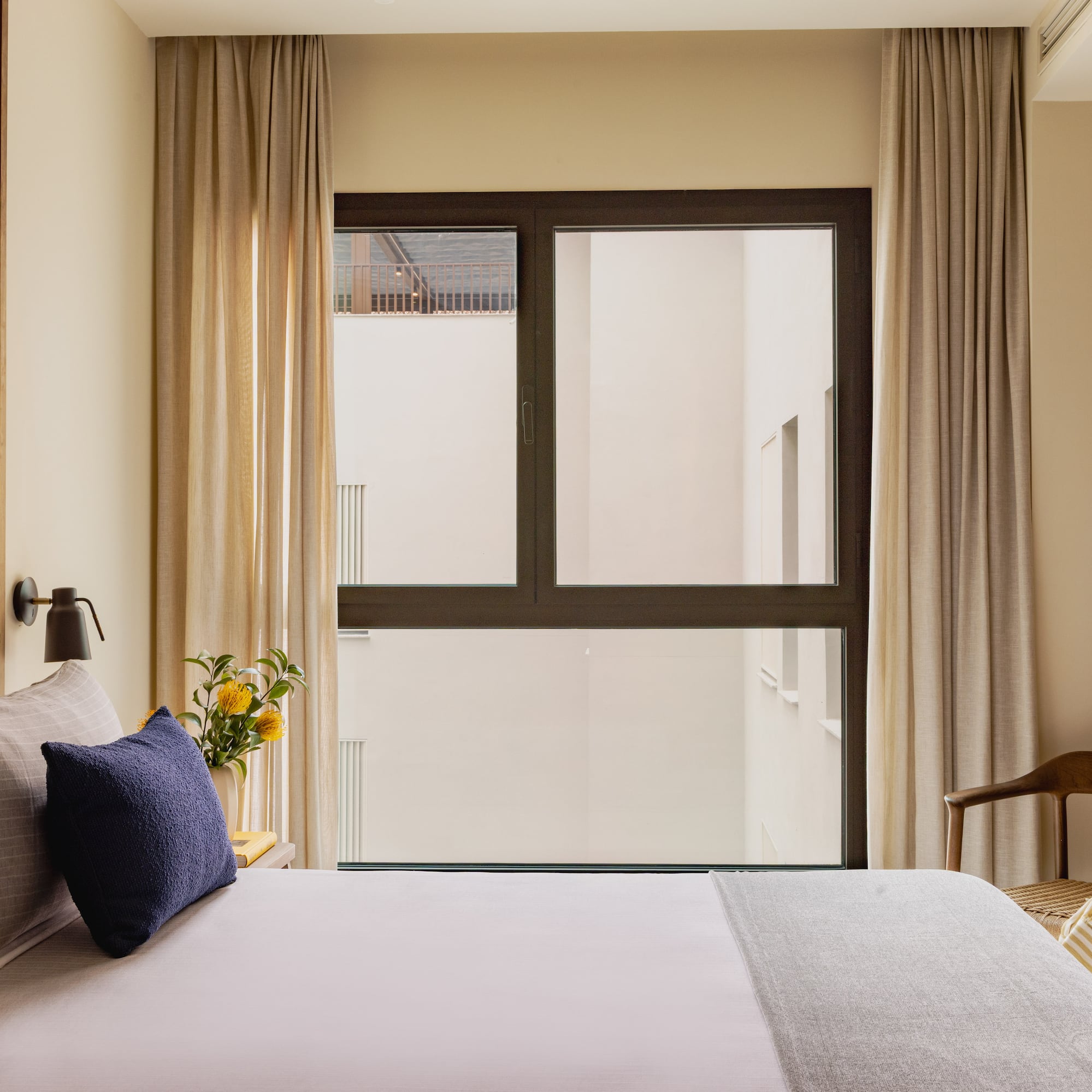 Modern hotel bedroom with wooden headboard, navy pillows, and large window.