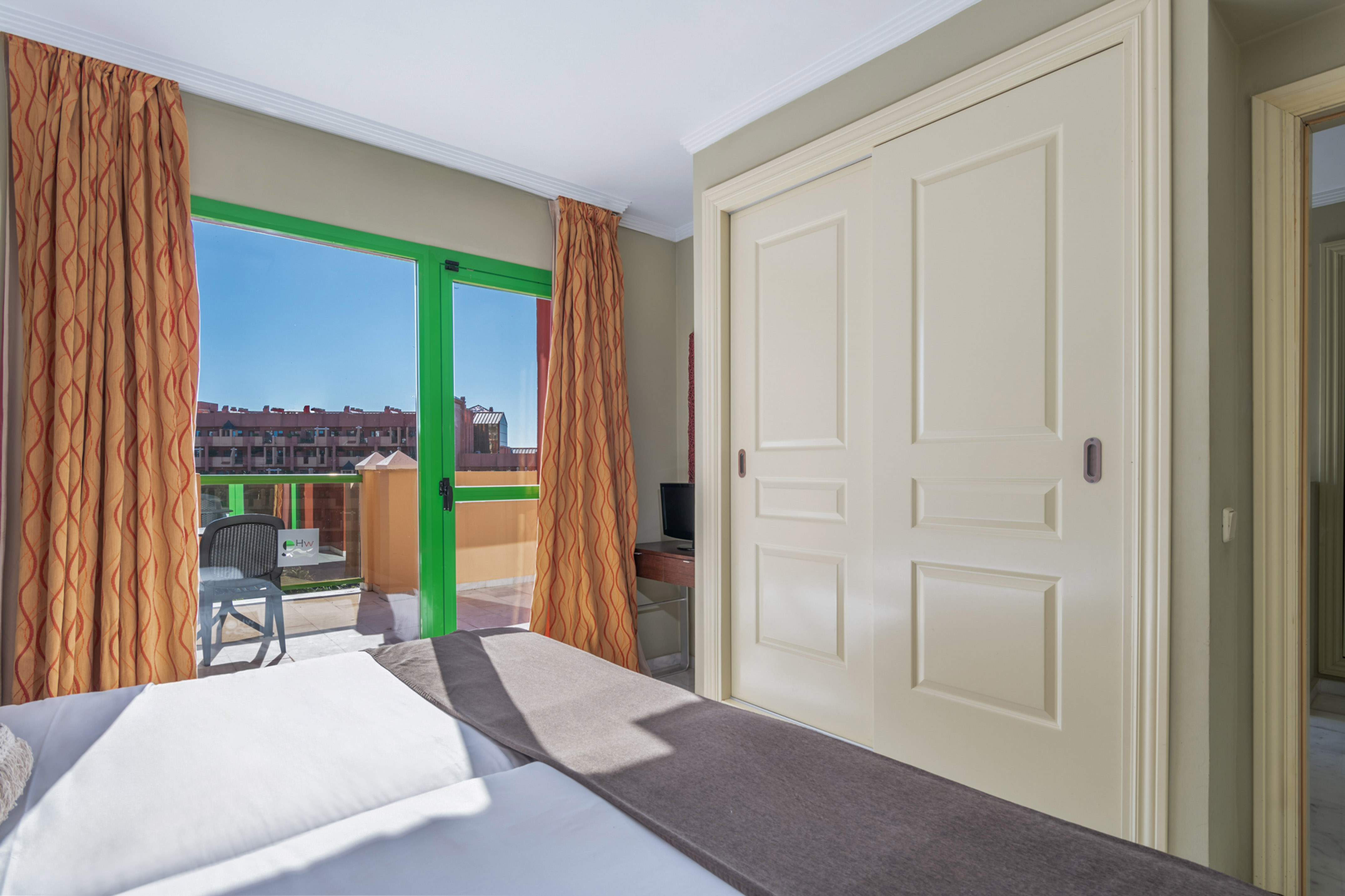Bright bedroom with green-framed balcony door, city view, and sliding wardrobe.