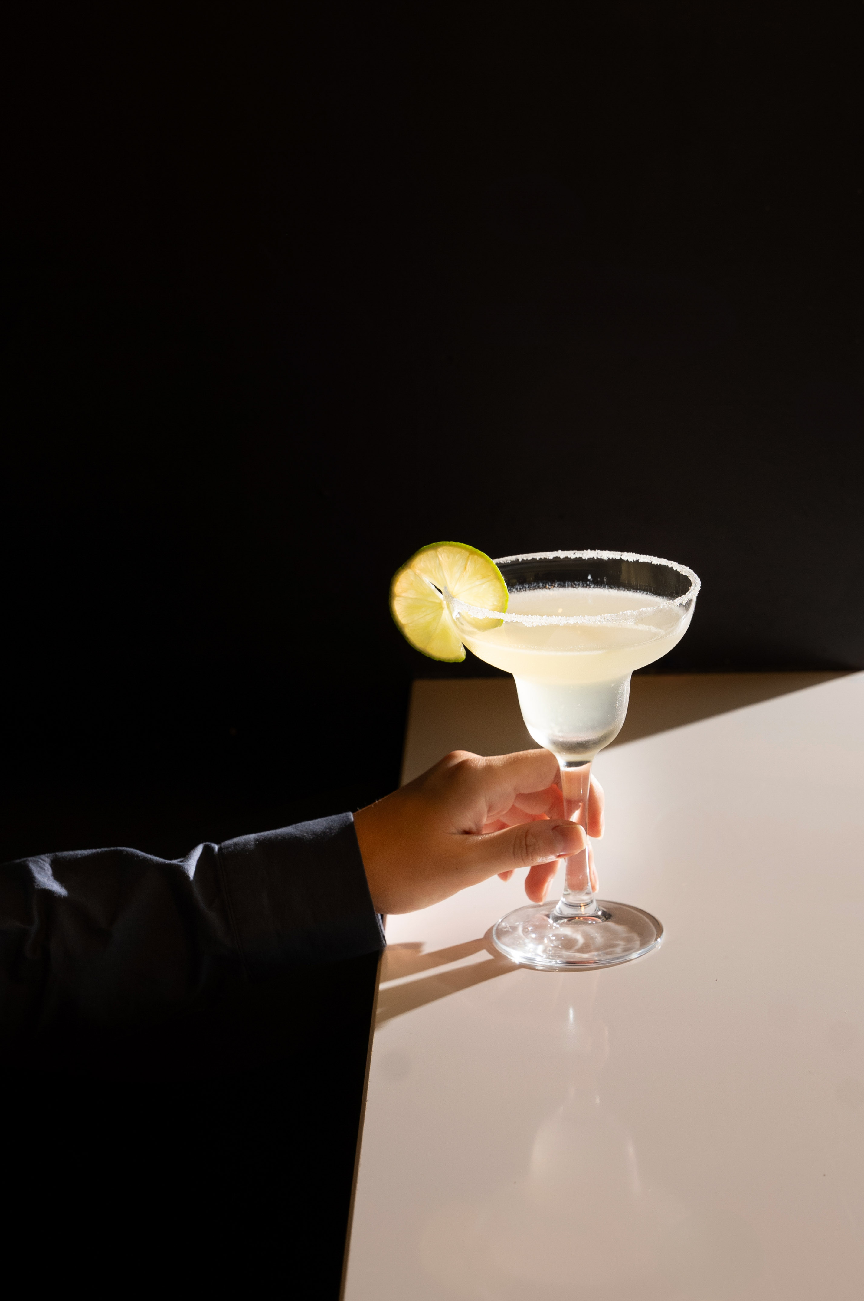 Margarita with lime, salted rim, held by a hand.