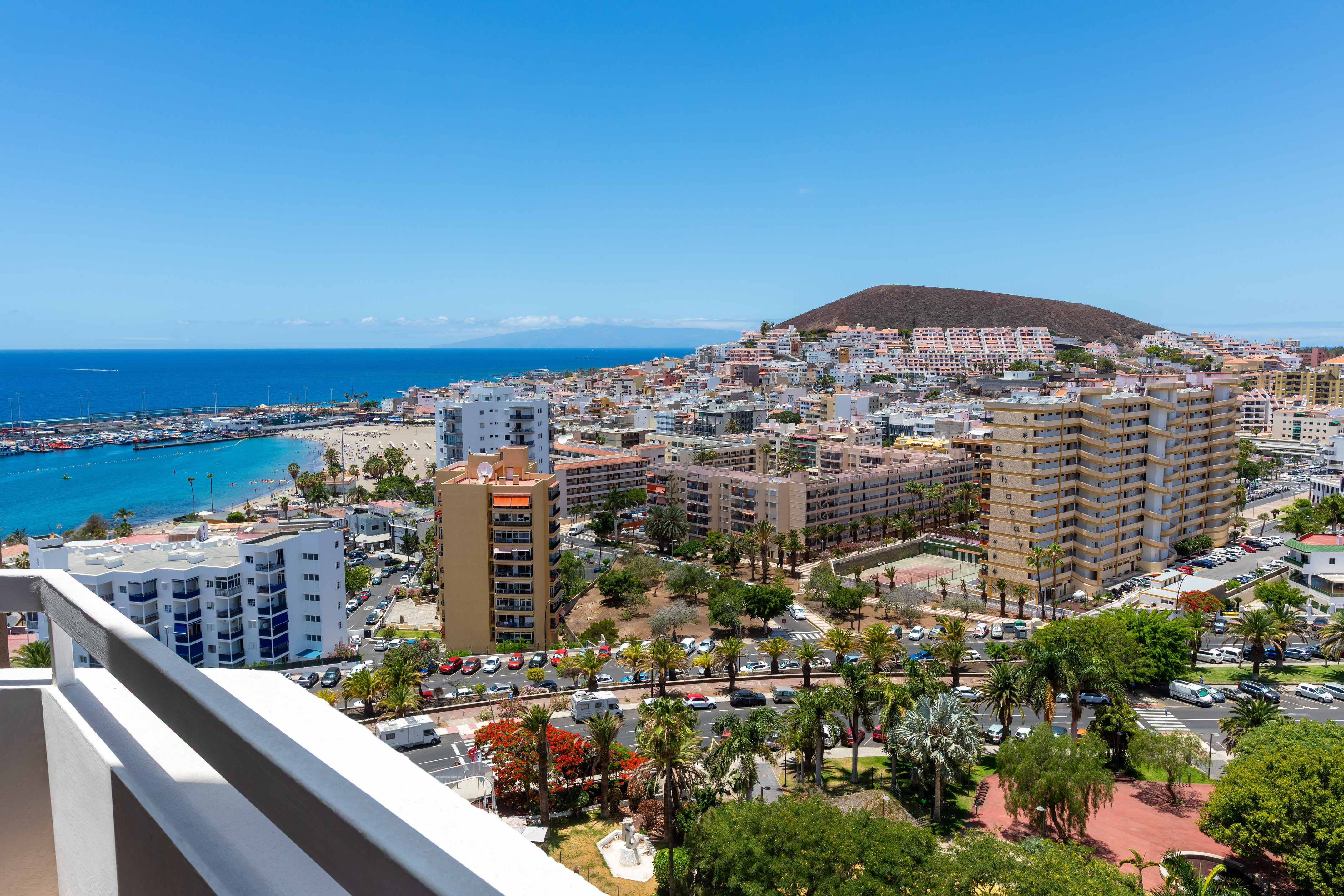 Coastal resort panorama: beach, marina, hotels, city buildings, and hill.