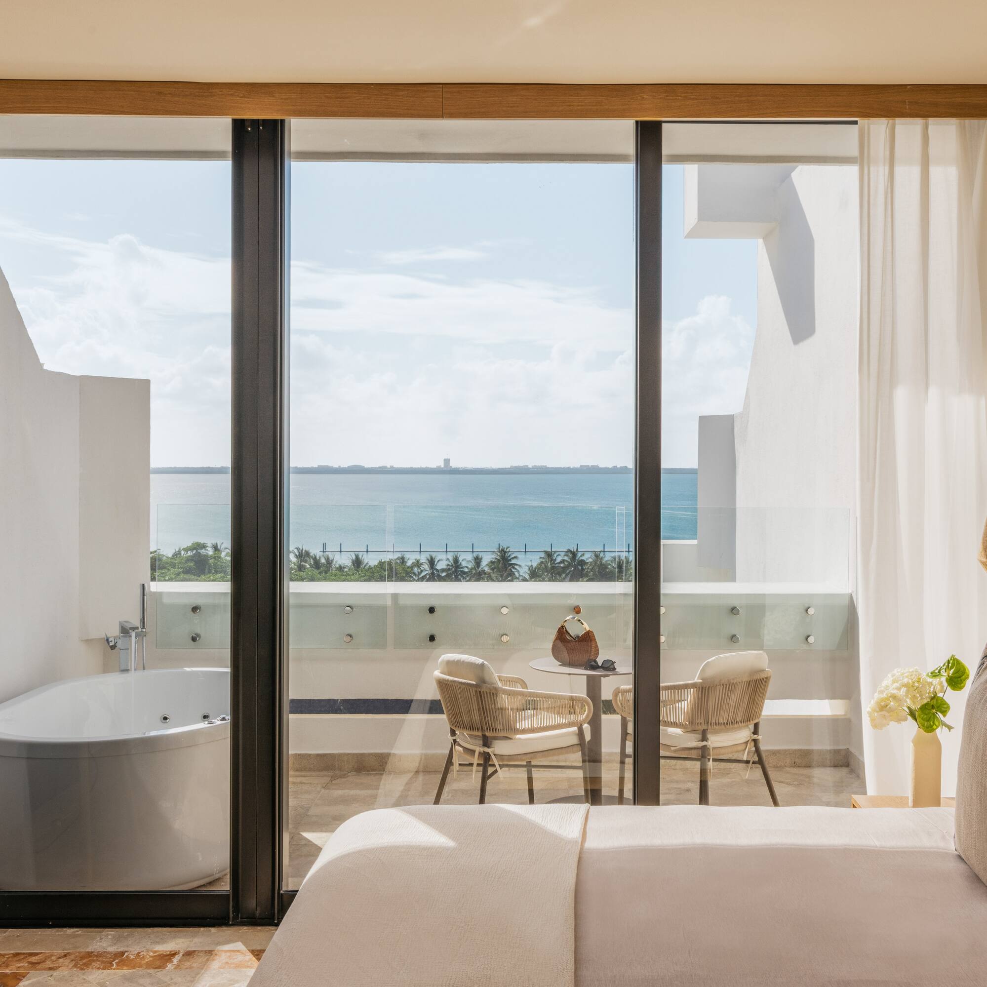 Ocean view hotel bedroom with balcony, outdoor jacuzzi tub, and seating.