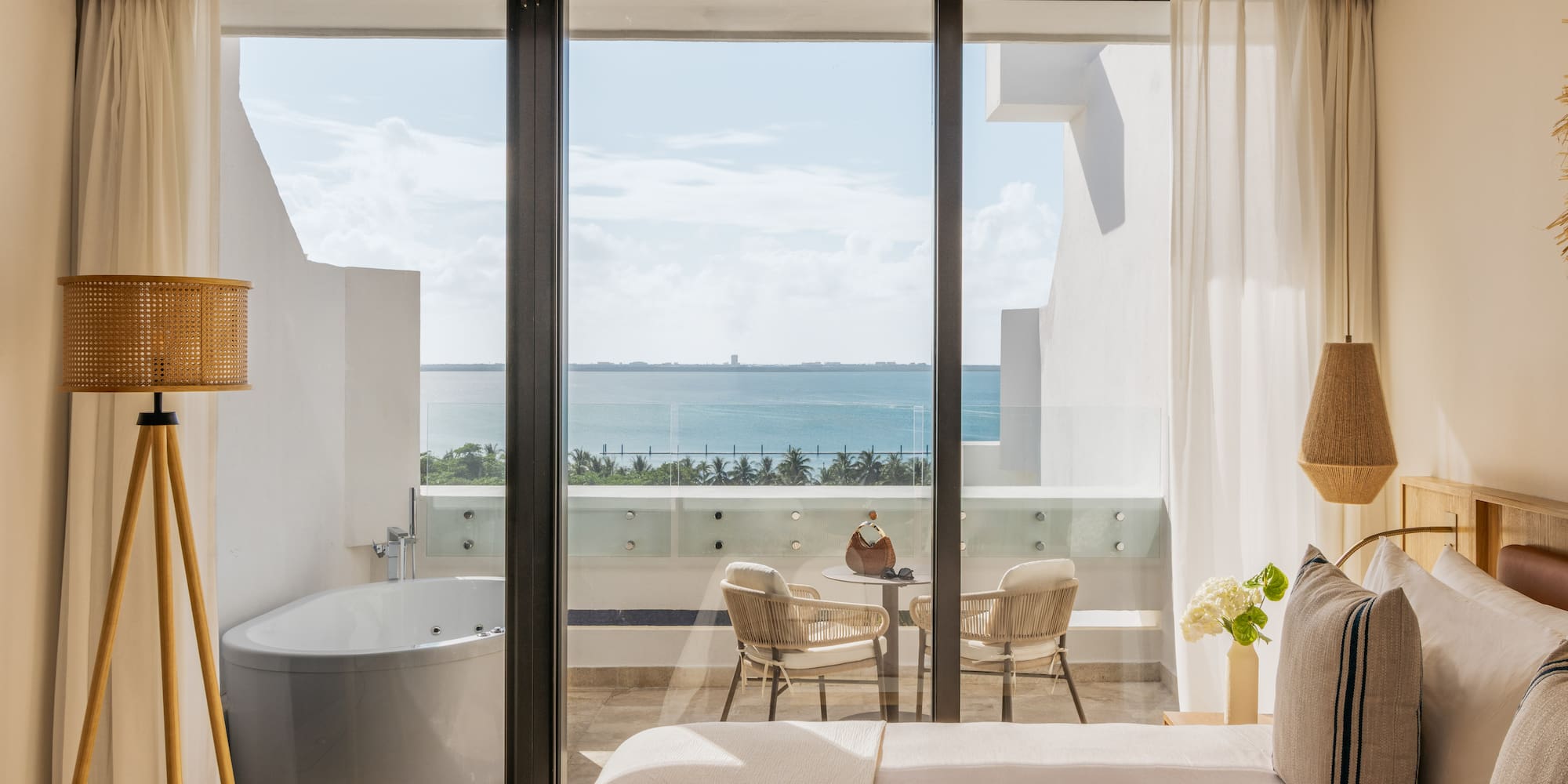 Ocean view hotel bedroom with balcony, outdoor jacuzzi tub, and seating.