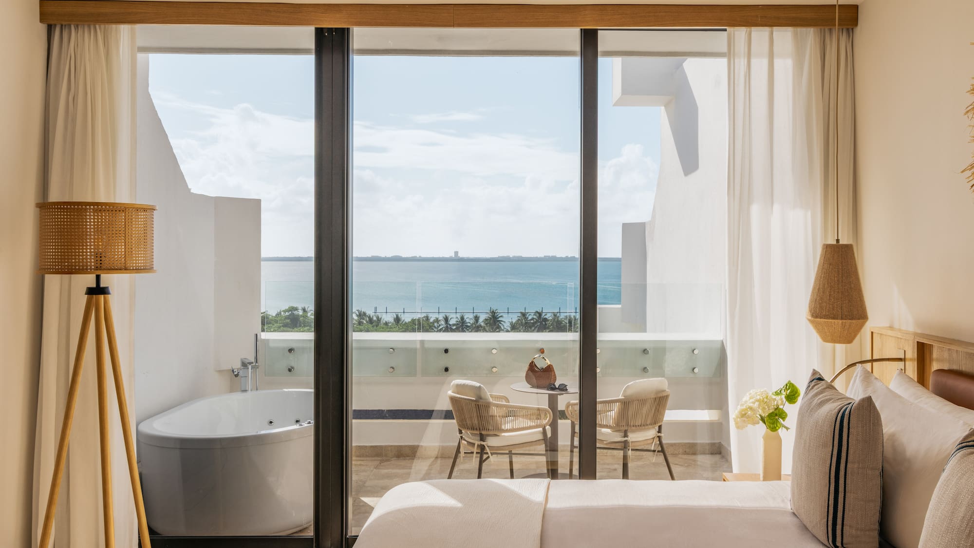 Ocean view hotel bedroom with balcony, outdoor jacuzzi tub, and seating.