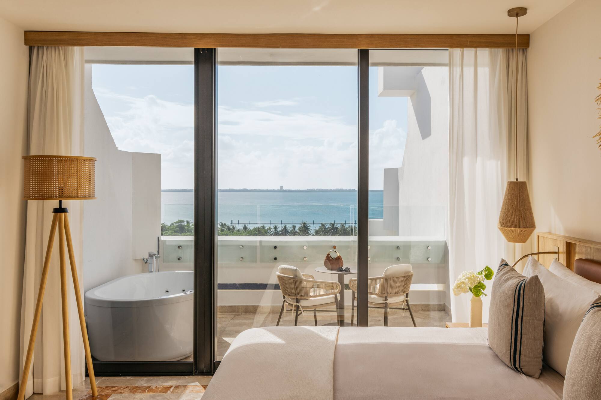 Ocean view hotel bedroom with balcony, outdoor jacuzzi tub, and seating.
