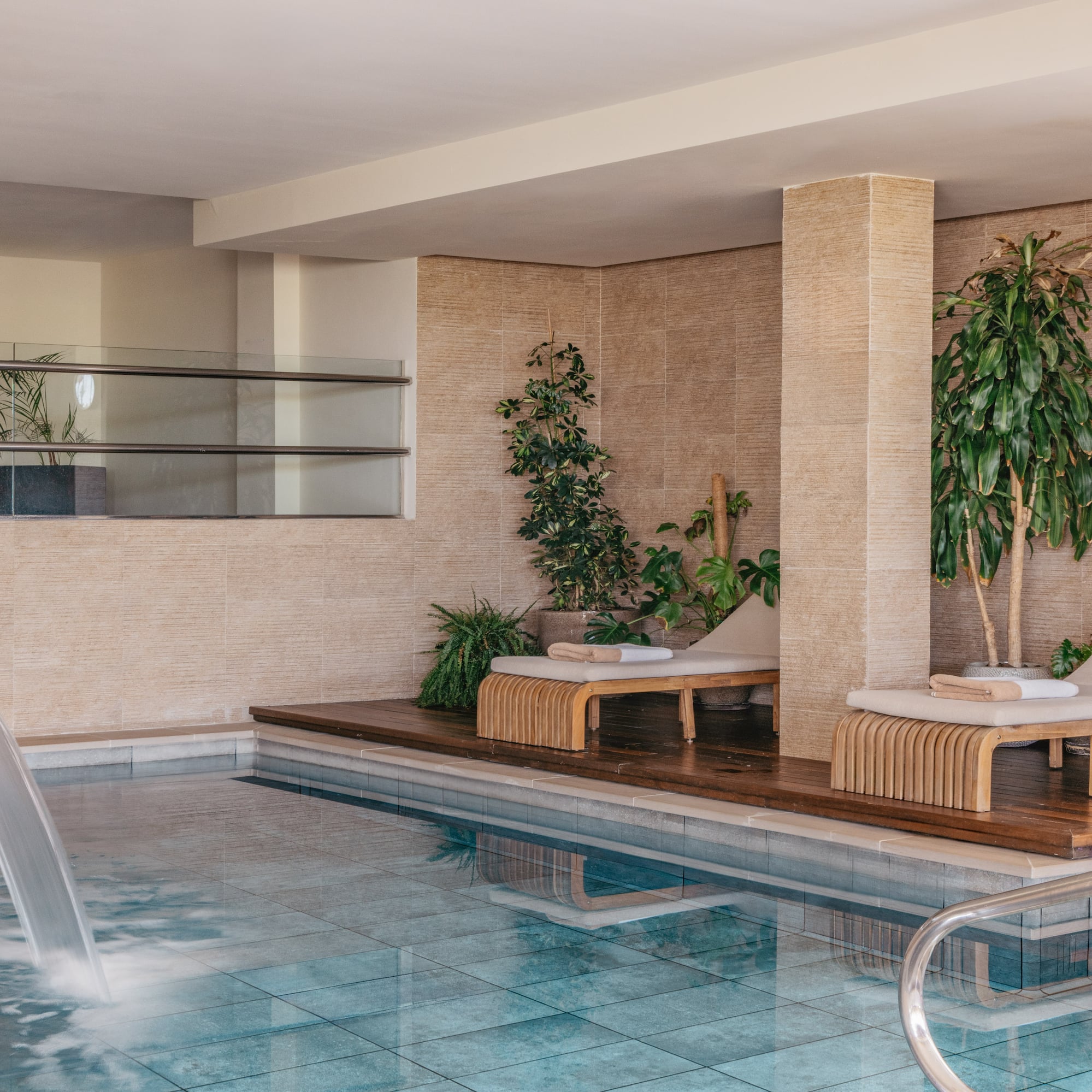Indoor spa pool with waterfall, wooden loungers, and tropical plants.
