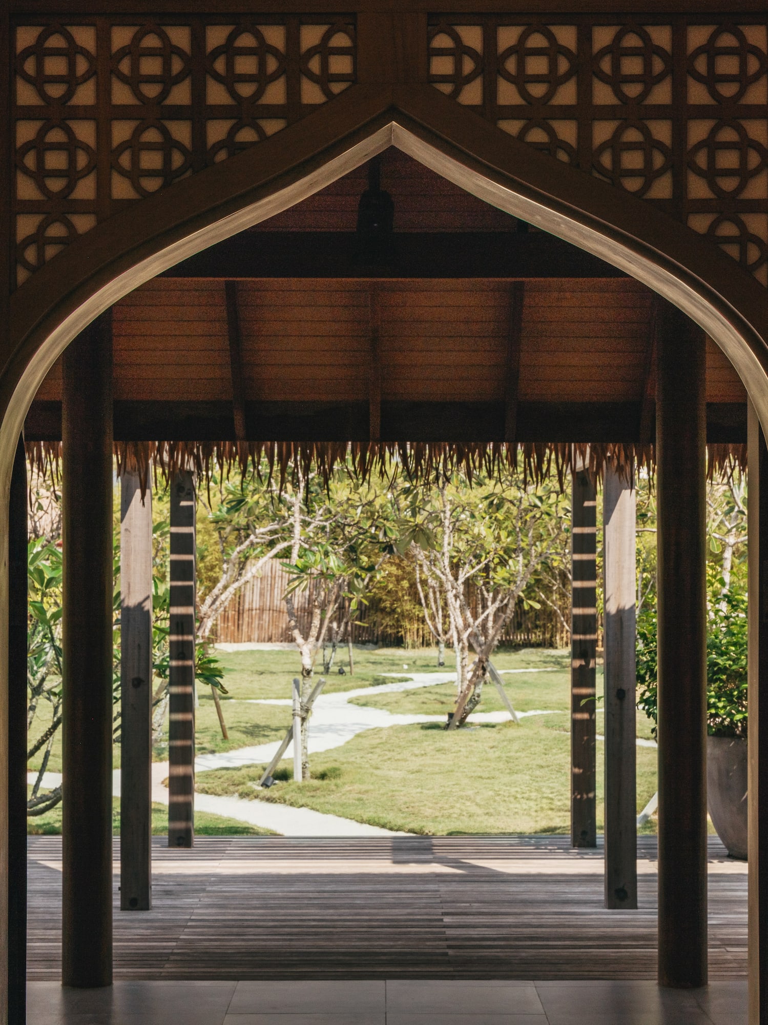 Arco de madera tallada con celosía geométrica a jardín tropical.