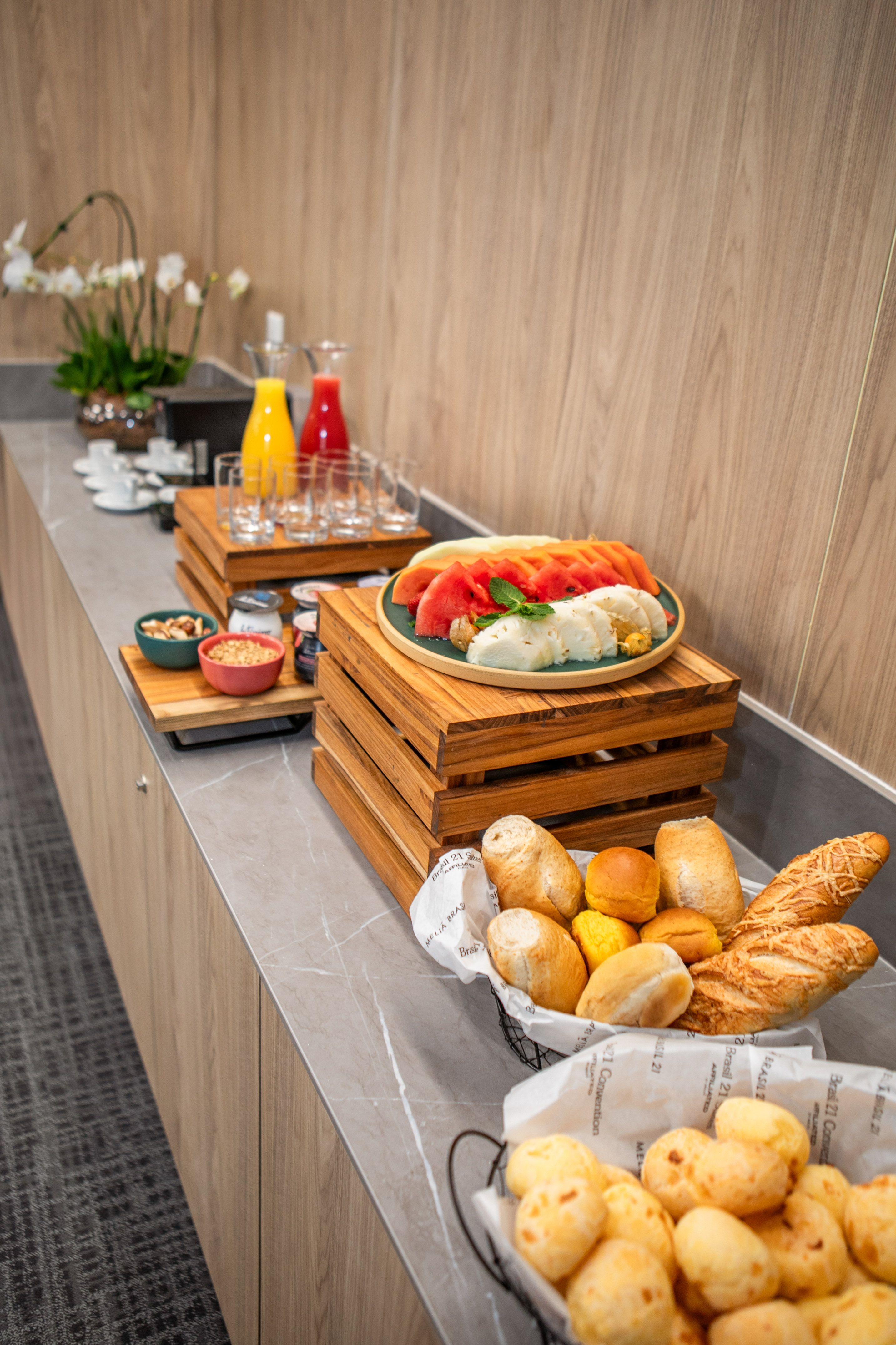 Hotel breakfast buffet: fresh fruit, assorted bread, Pão de queijo, and juices.