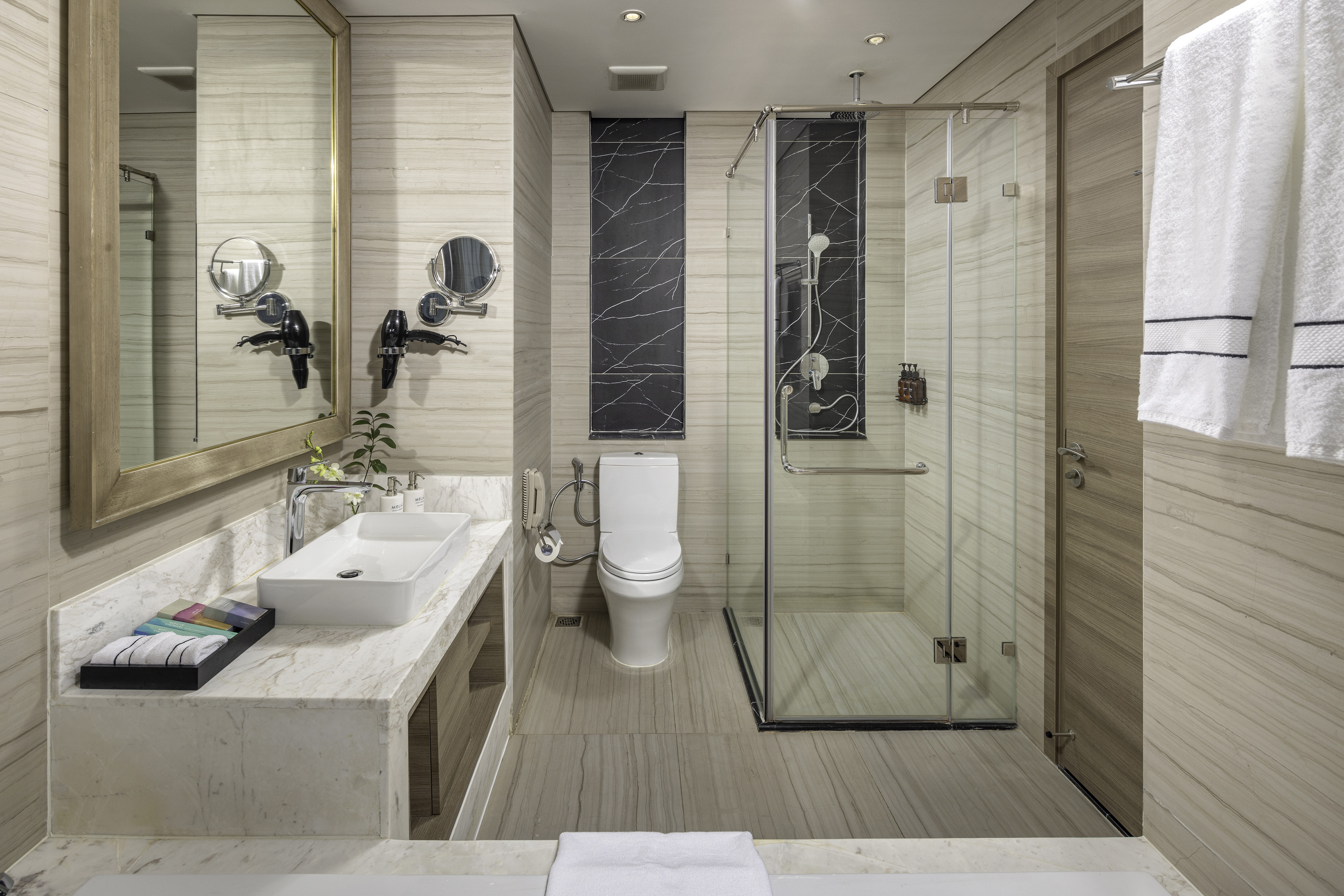 Modern hotel bathroom with marble vanity, rectangular sink, toilet, and glass shower.