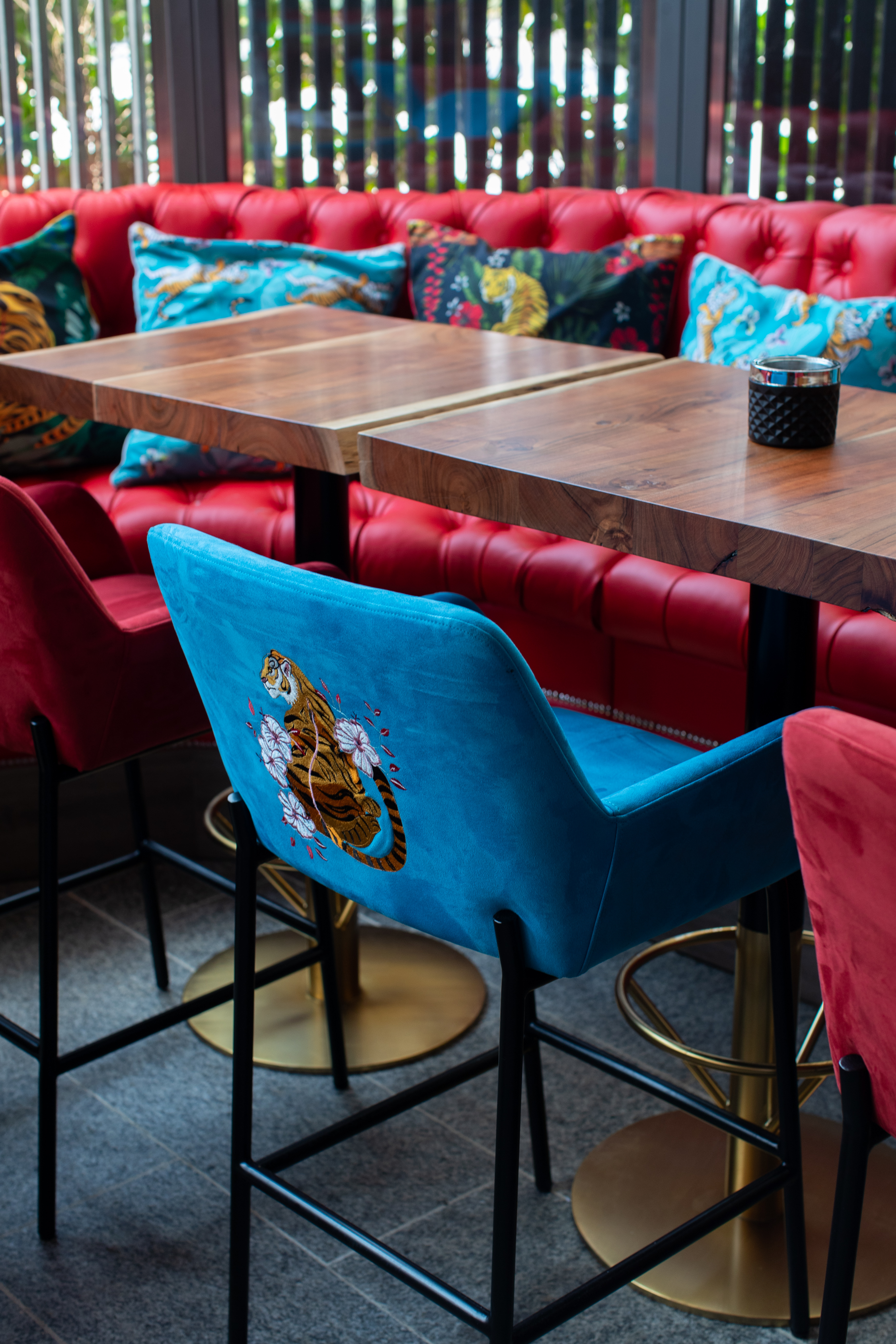Red tufted booth, wooden tables, blue velvet tiger bar stools.