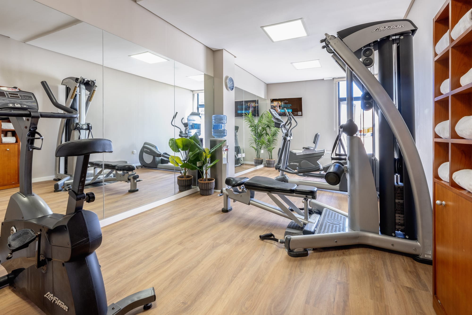 Modern fitness center with cardio and weight machines, large mirrors, and wood floor.