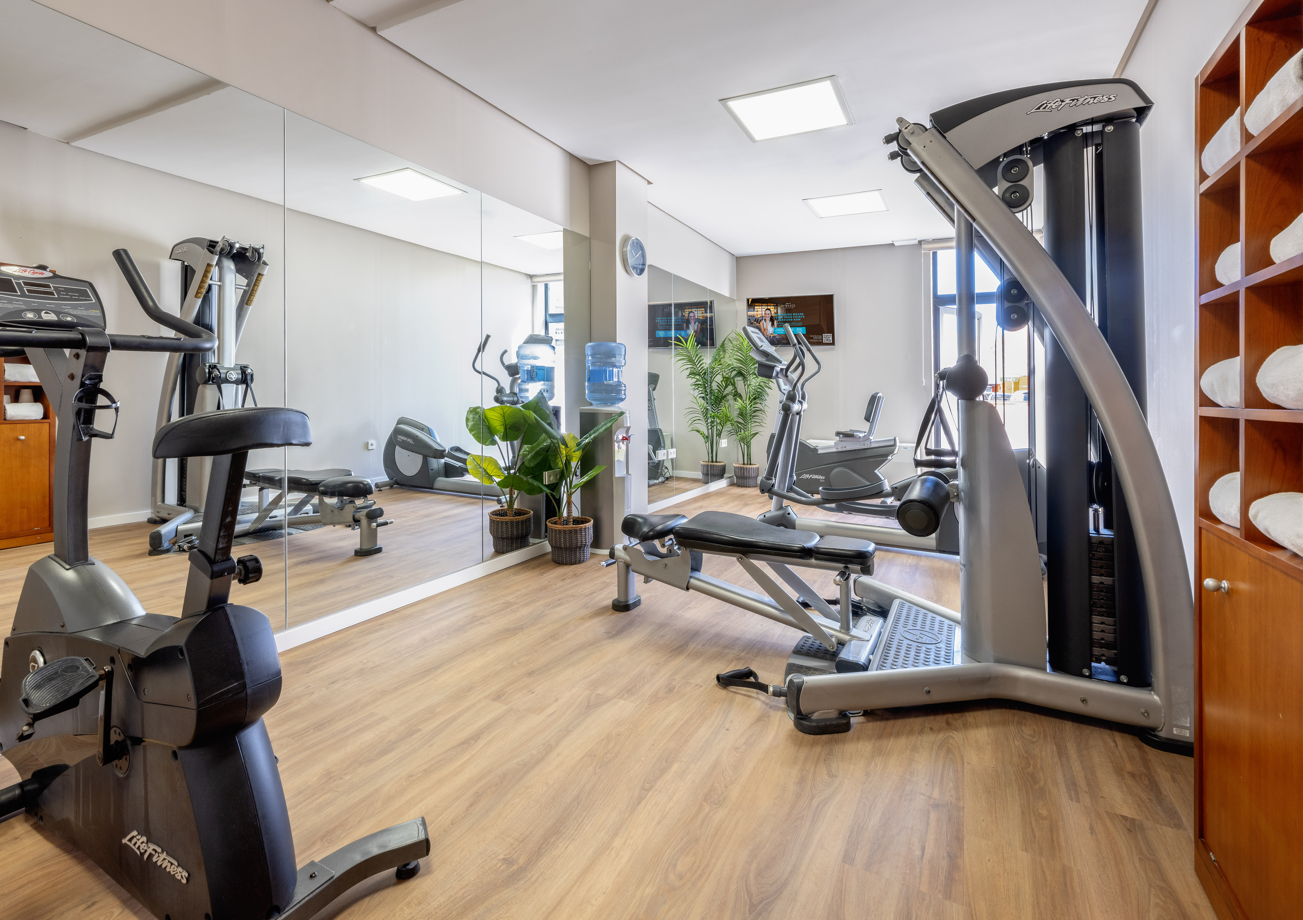 Modern fitness center with cardio and weight machines, large mirrors, and wood floor.