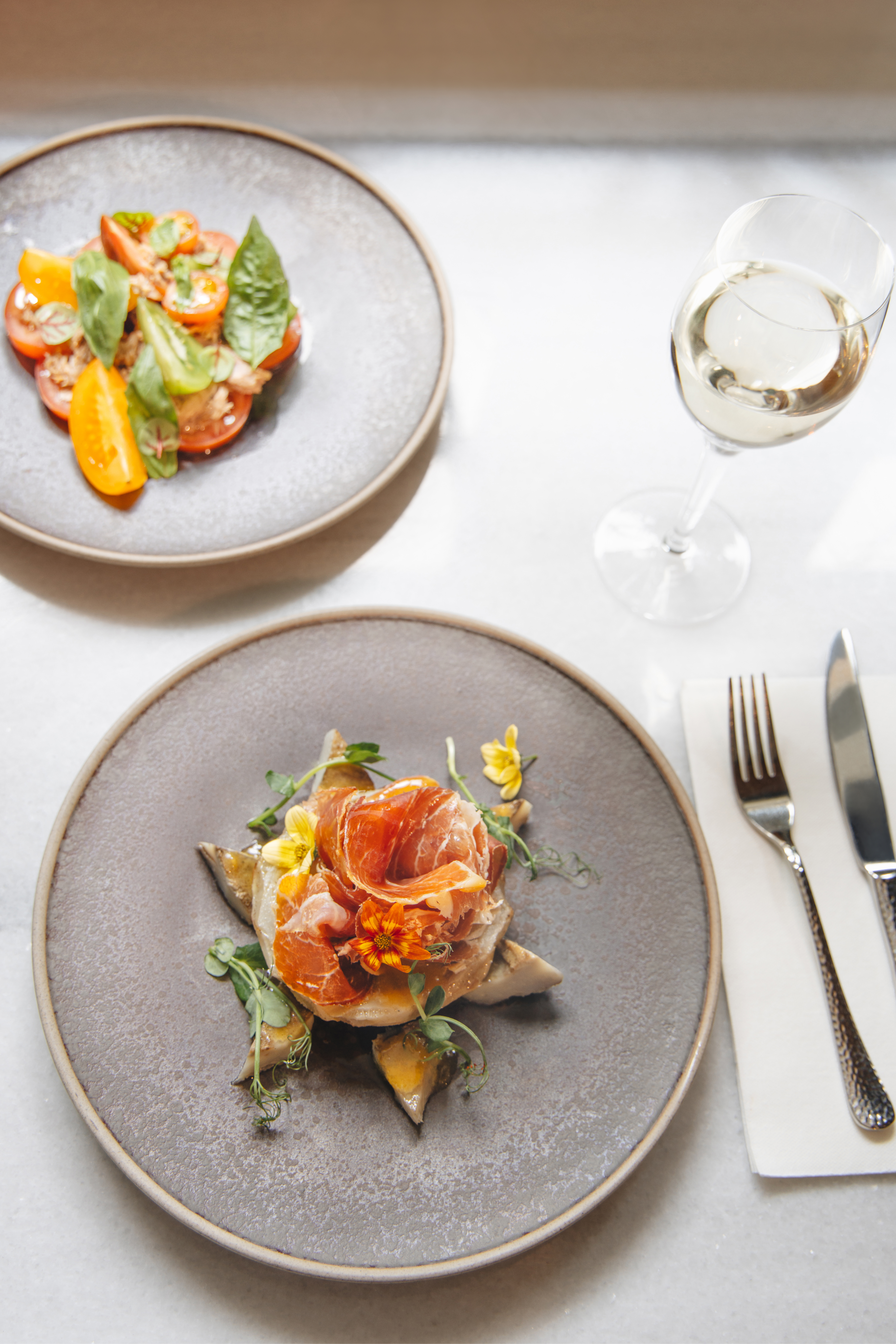 Gourmet prosciutto appetizer, tomato basil salad, and white wine.