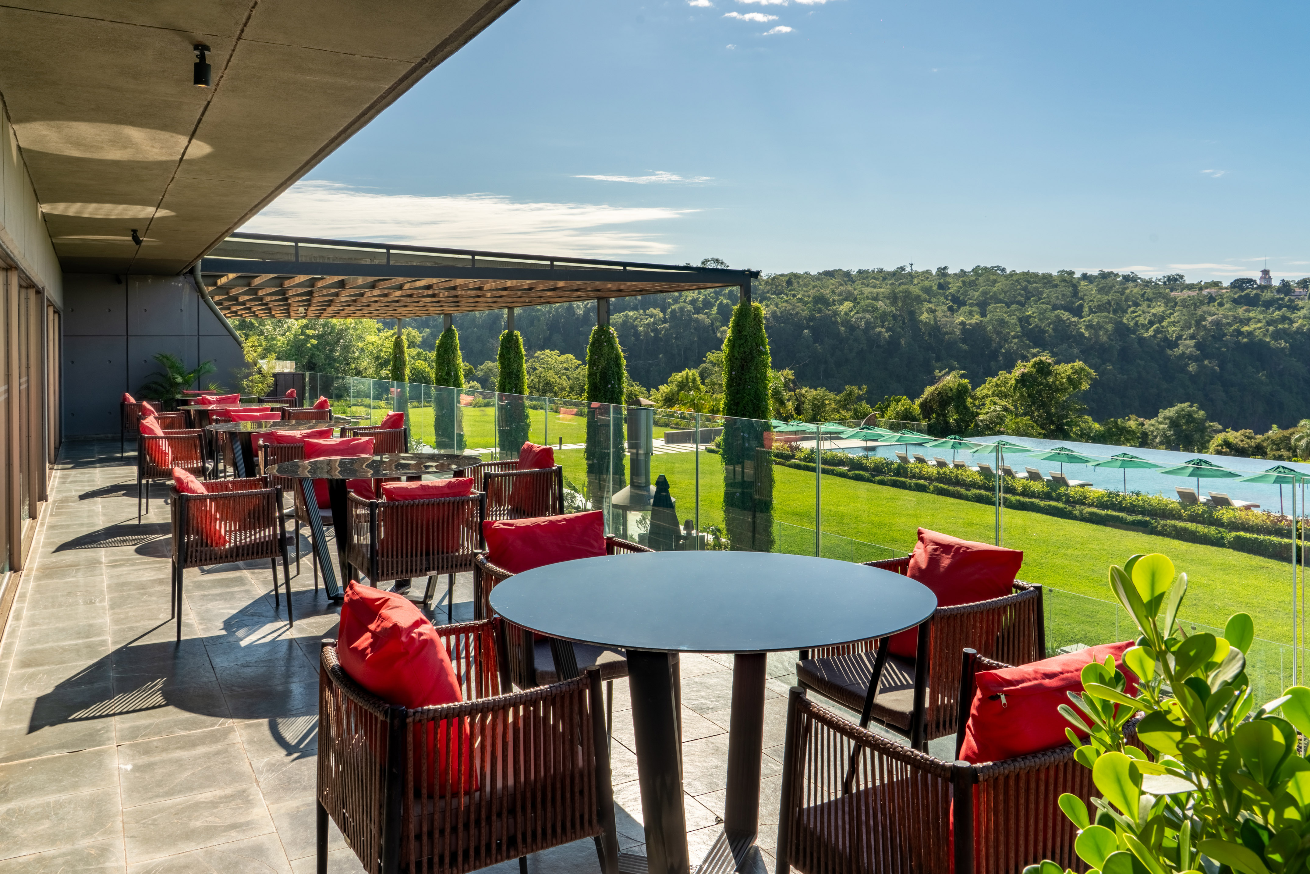 Outdoor restaurant terrace with red chairs, jungle view, and infinity pool.