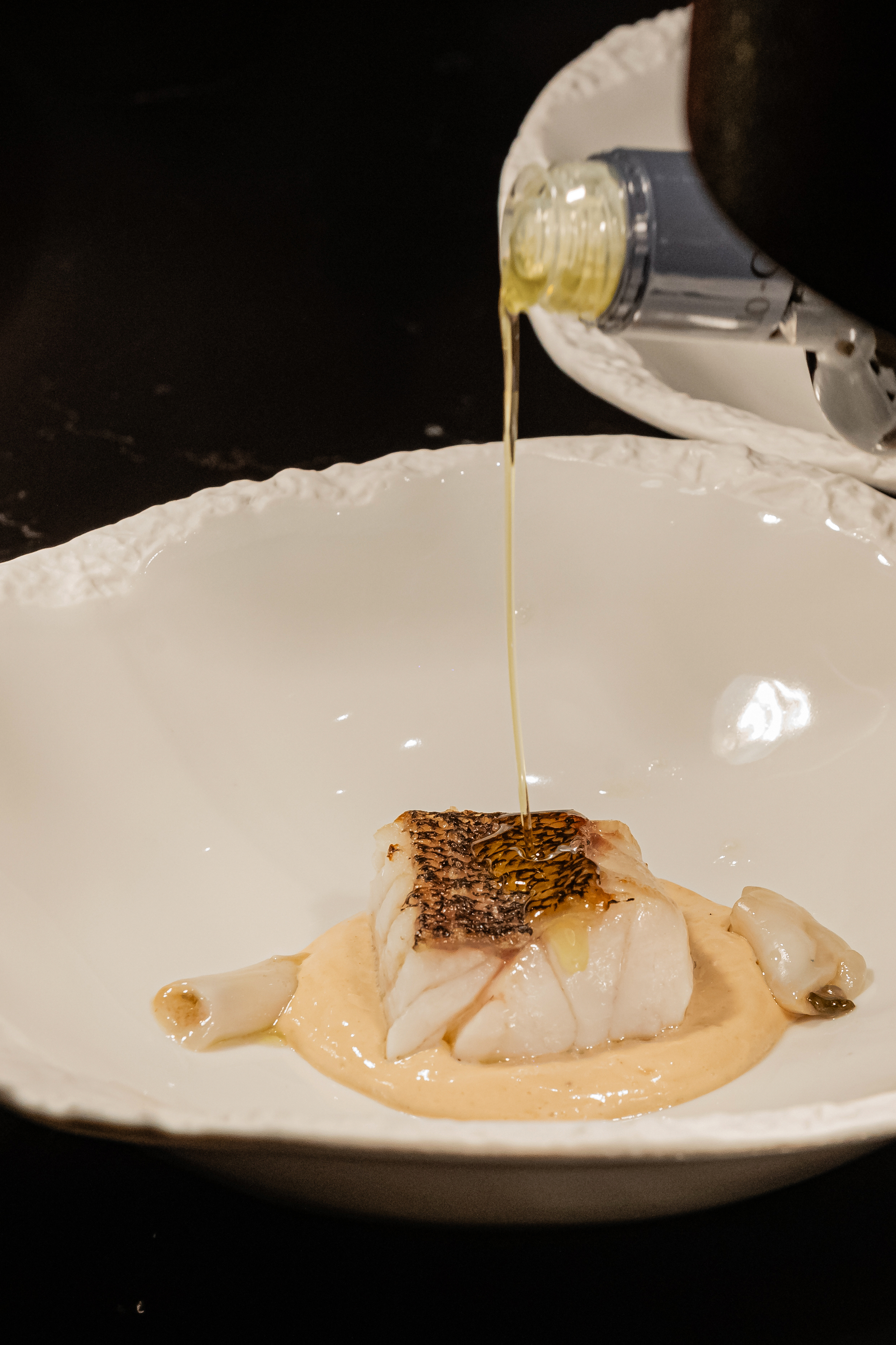 Seared fish on creamy sauce, oil drizzling from bottle, elegant seafood plate.
