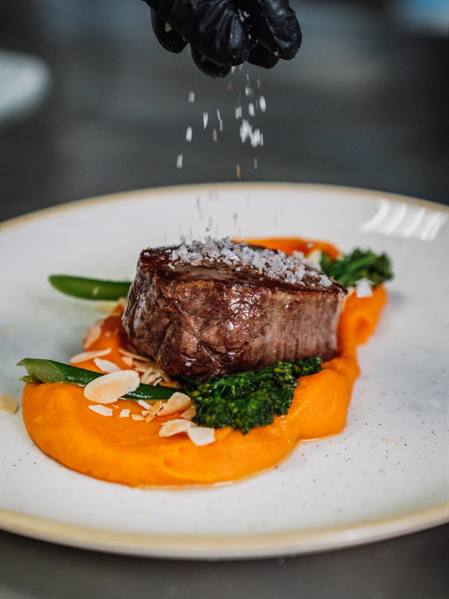 a hand sprinkling salt on a piece of meat on a plate