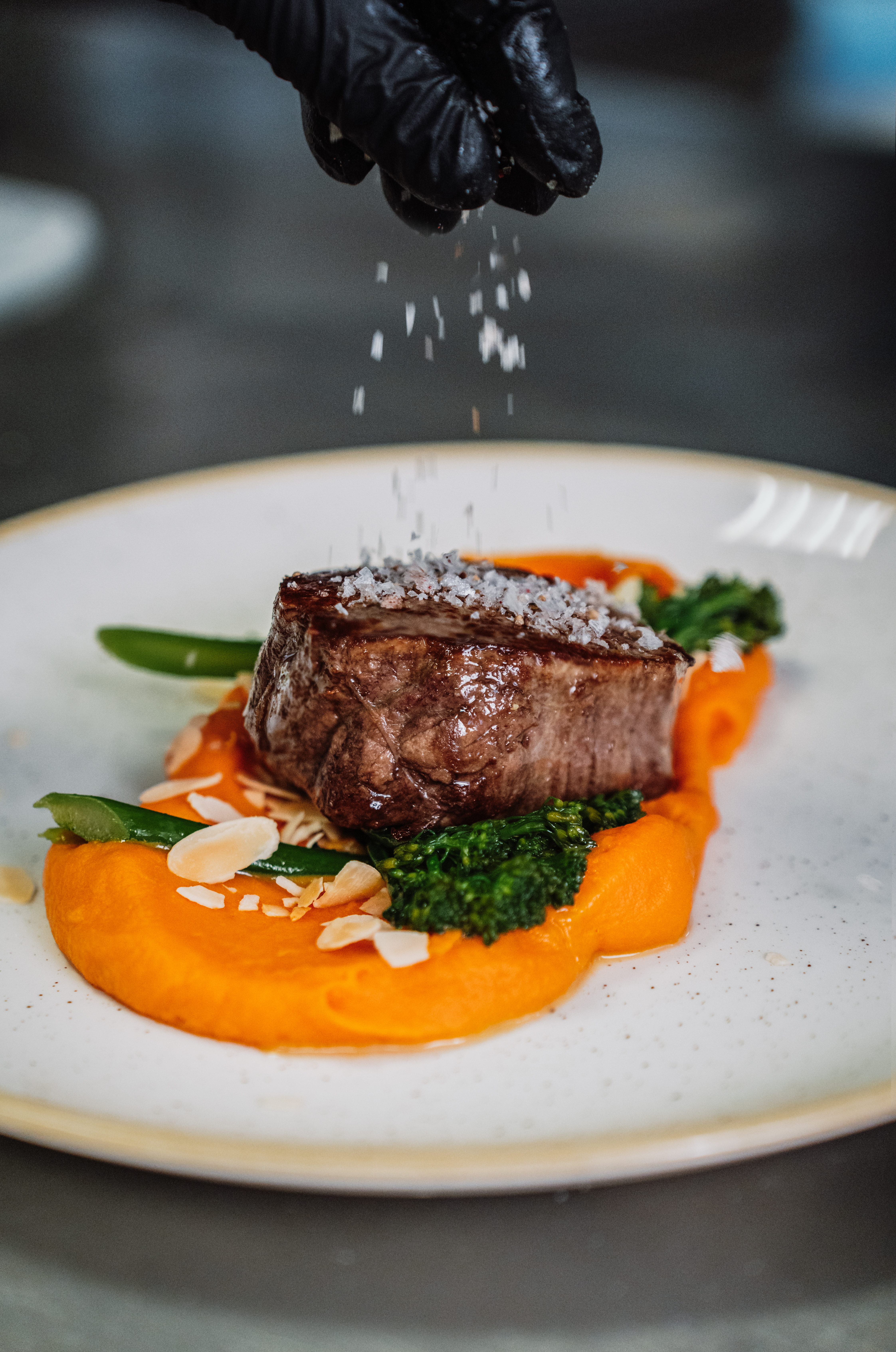 a hand sprinkling salt on a piece of meat on a plate