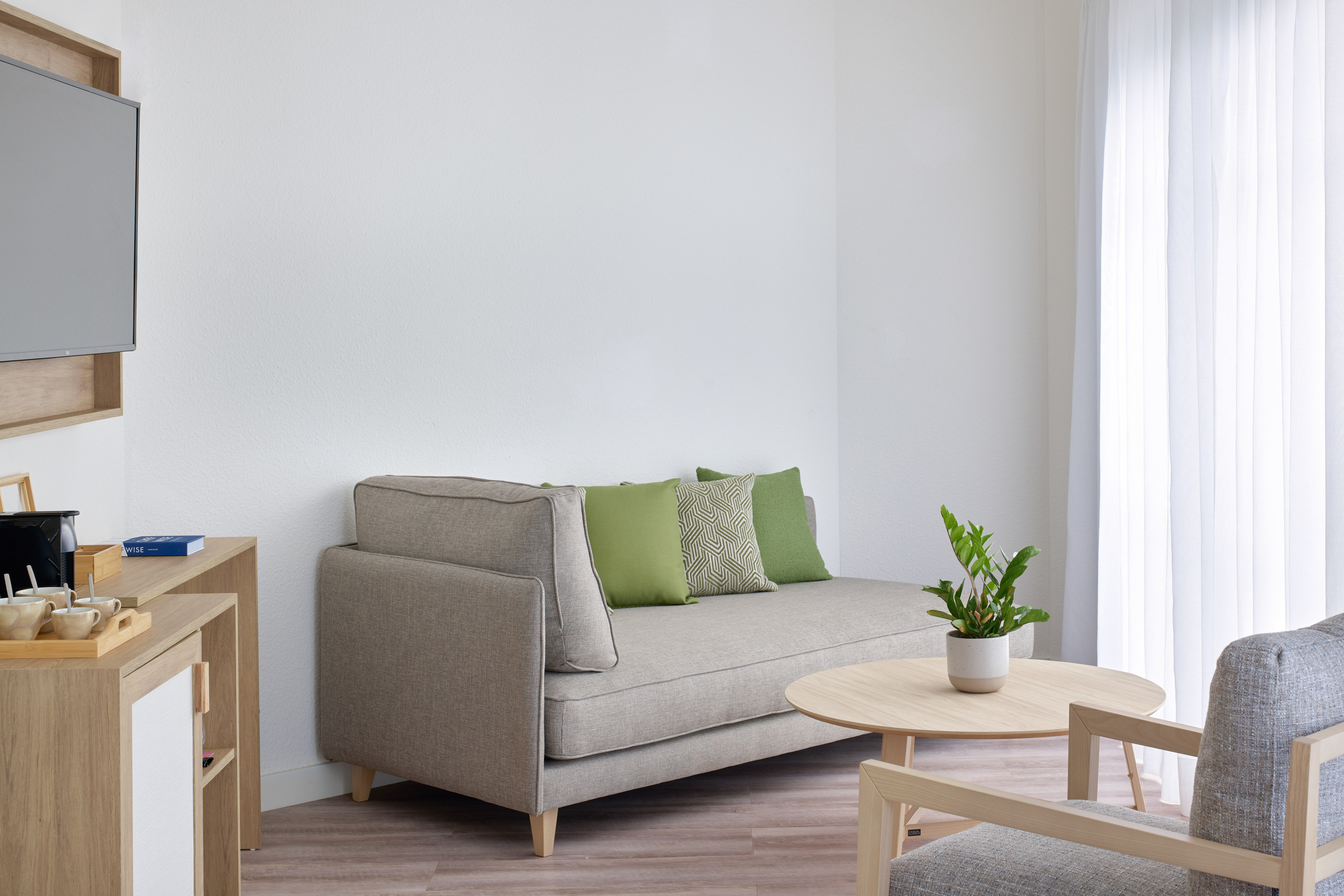 Contemporary living room: gray sofa, green pillows, wood coffee table, TV.