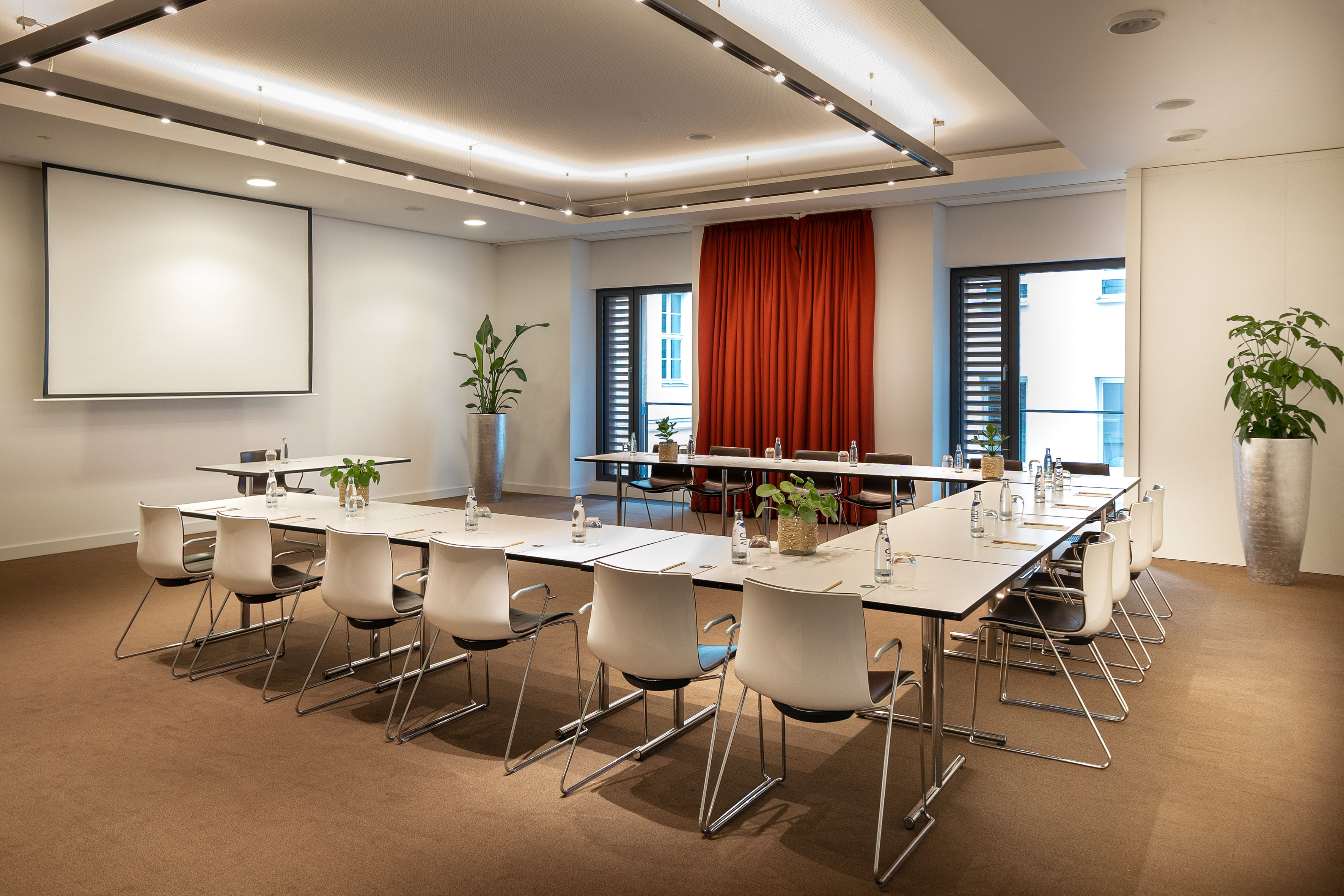 Modern U-shape conference room setup with projection screen, tables, and red curtains.