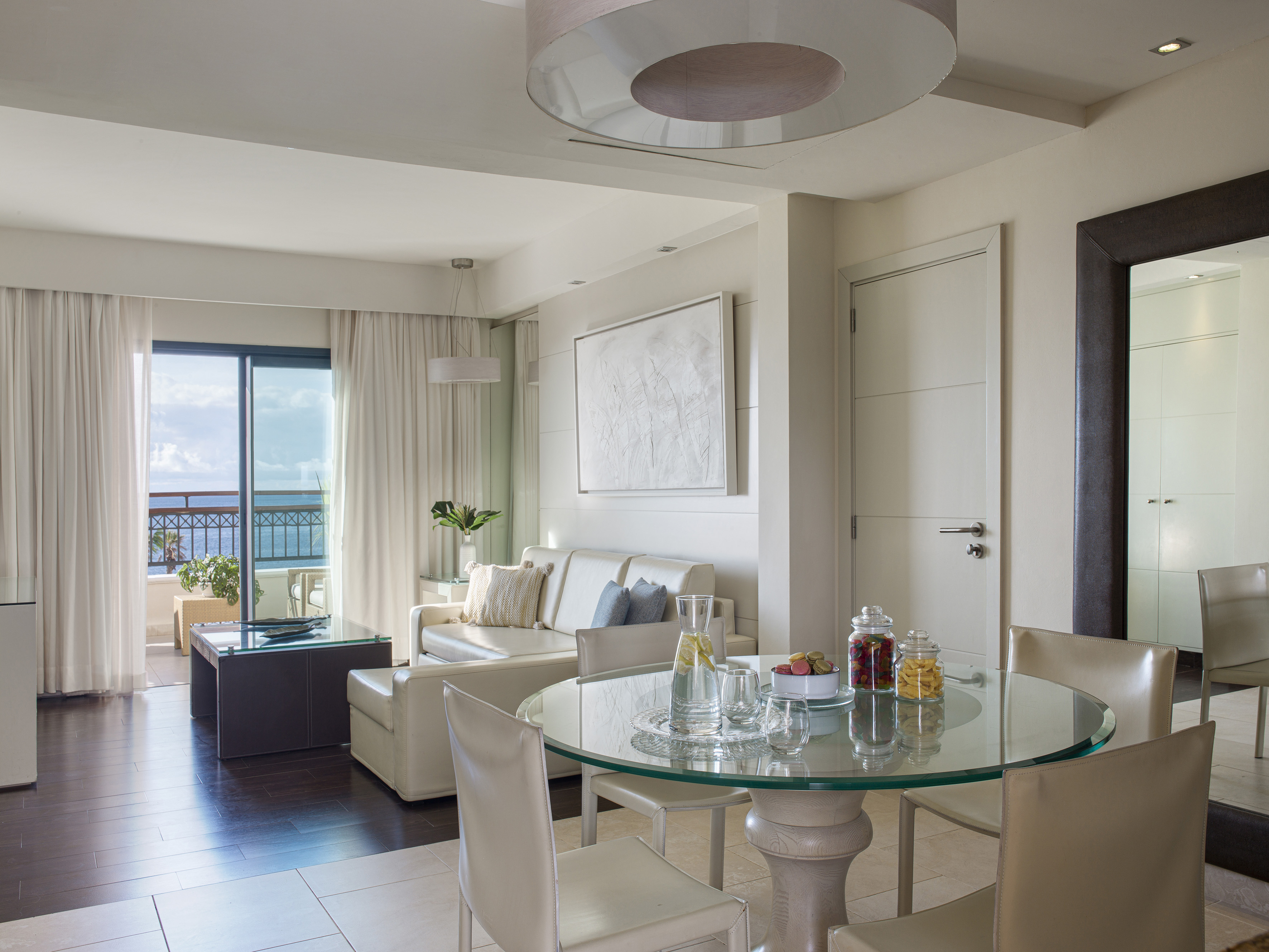 Elegant hotel suite living room with dining table and ocean view balcony.