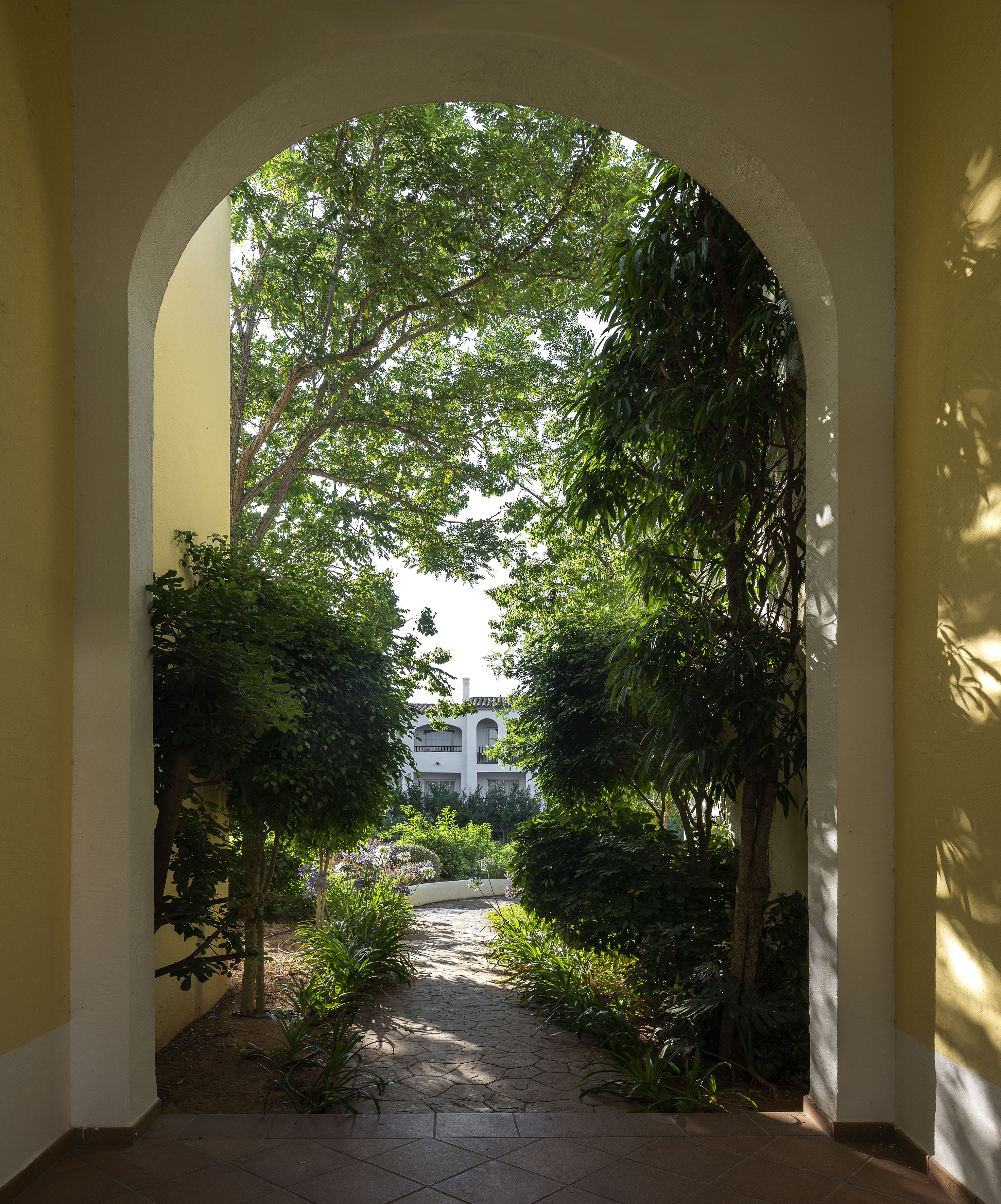 Yellow archway framing a lush green garden path and white resort building.