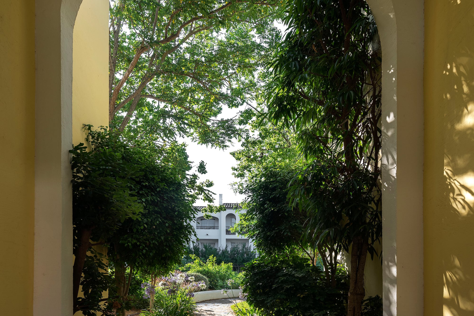 Yellow archway framing a lush green garden path and white resort building.