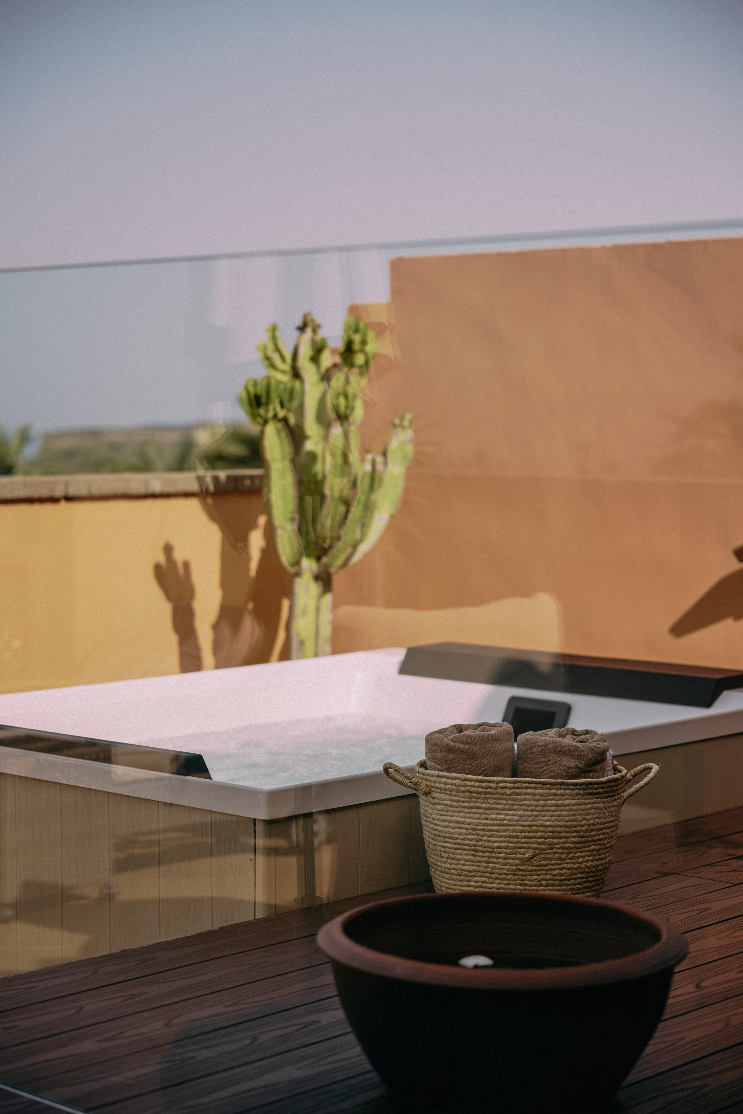 Outdoor hot tub on wooden deck with rolled towels in basket and desert cactus.