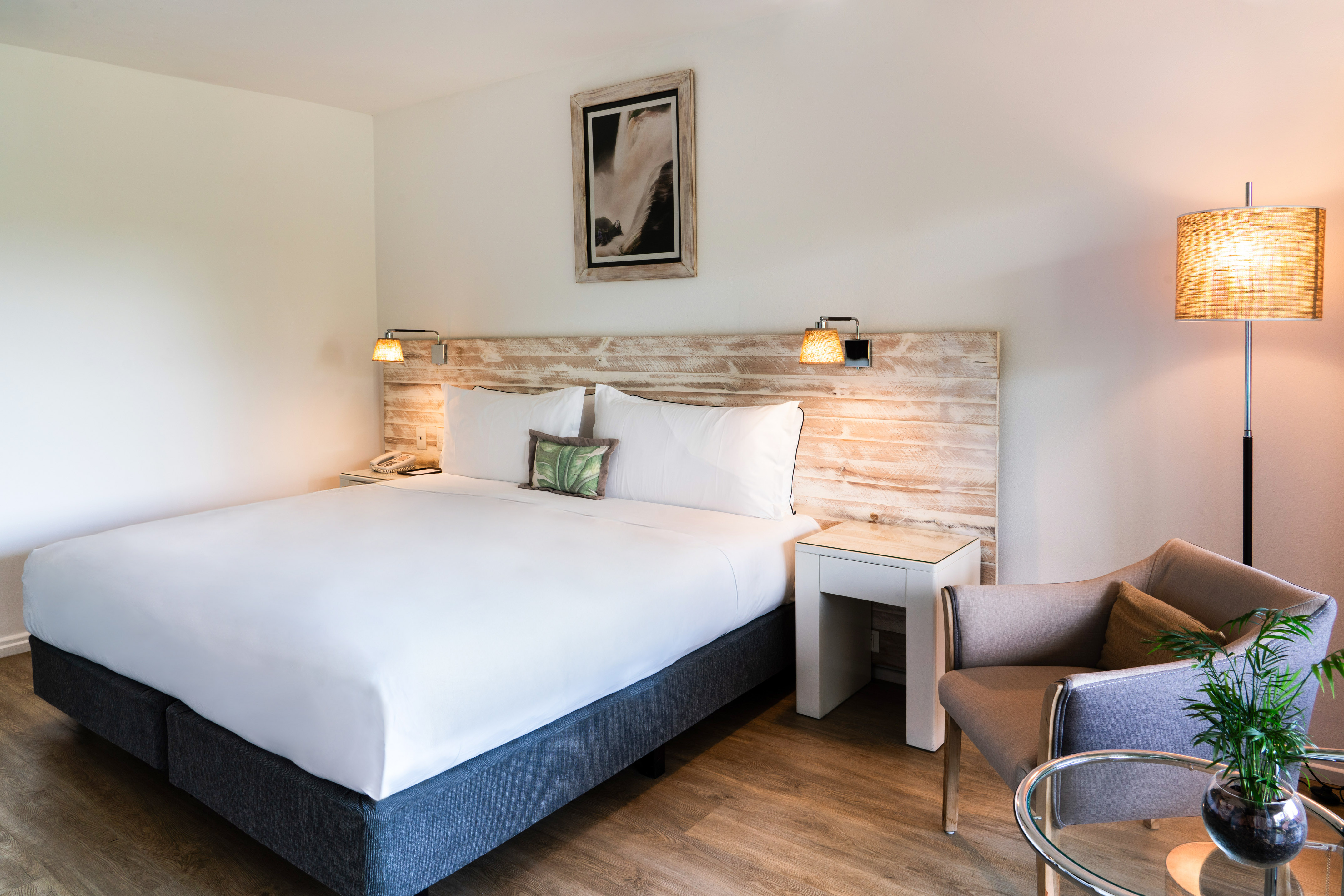 Comfortable hotel bedroom with king bed, rustic headboard, and cozy armchair.