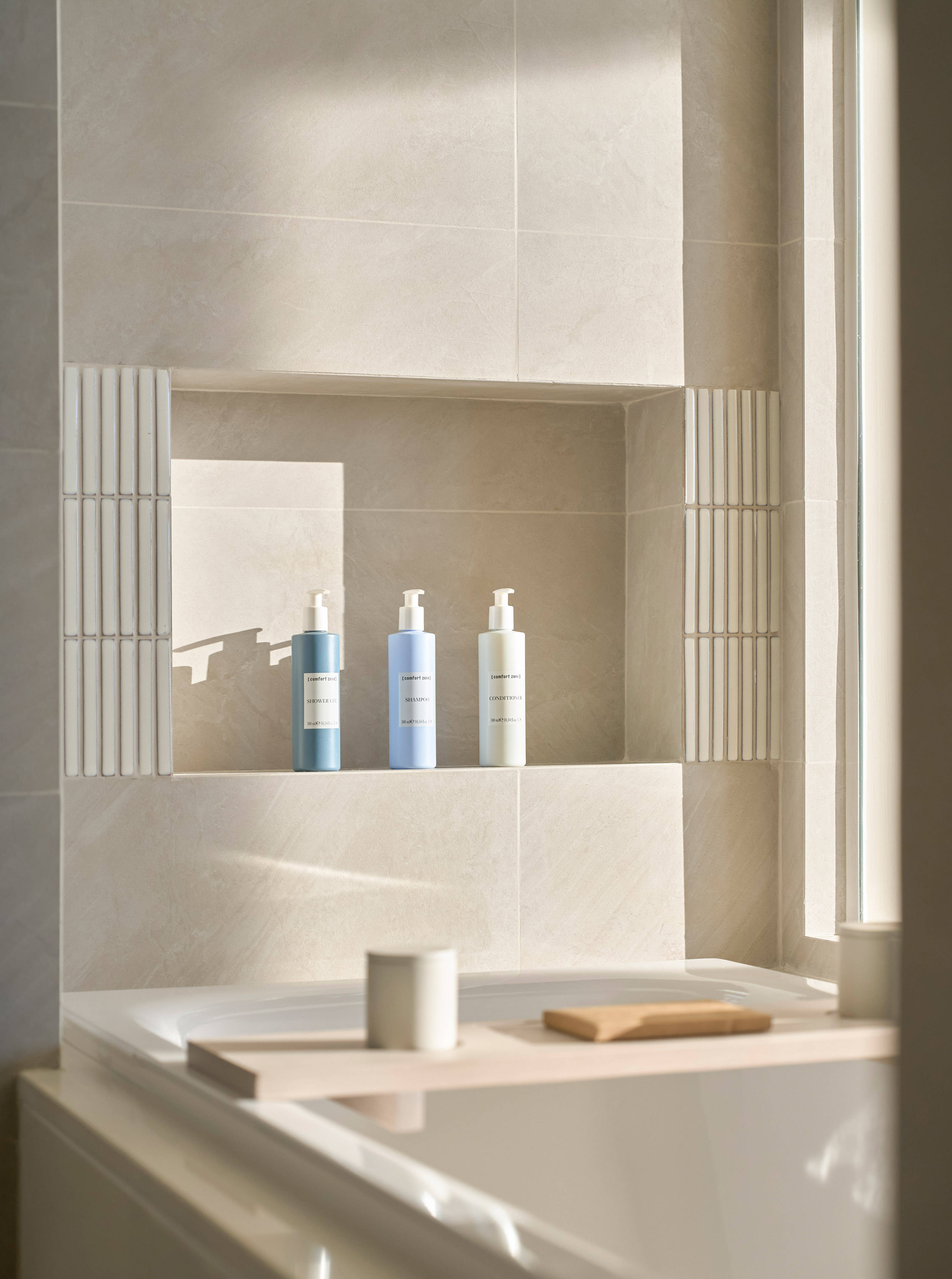 Tiled bathroom niche with minimalist toiletries above a modern bathtub with caddy.