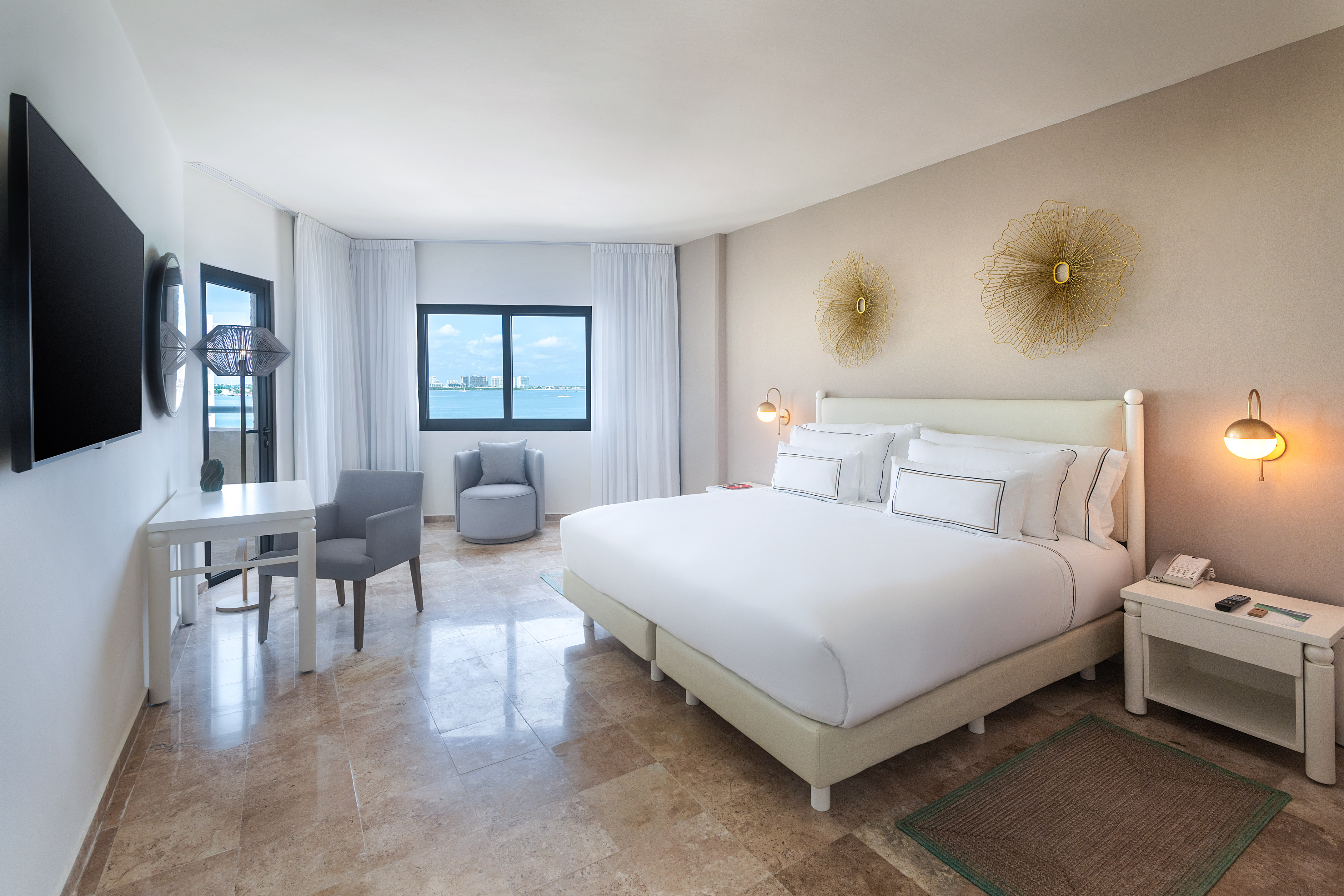 Modern hotel room with ocean view, king bed, work desk, and stylish decor.