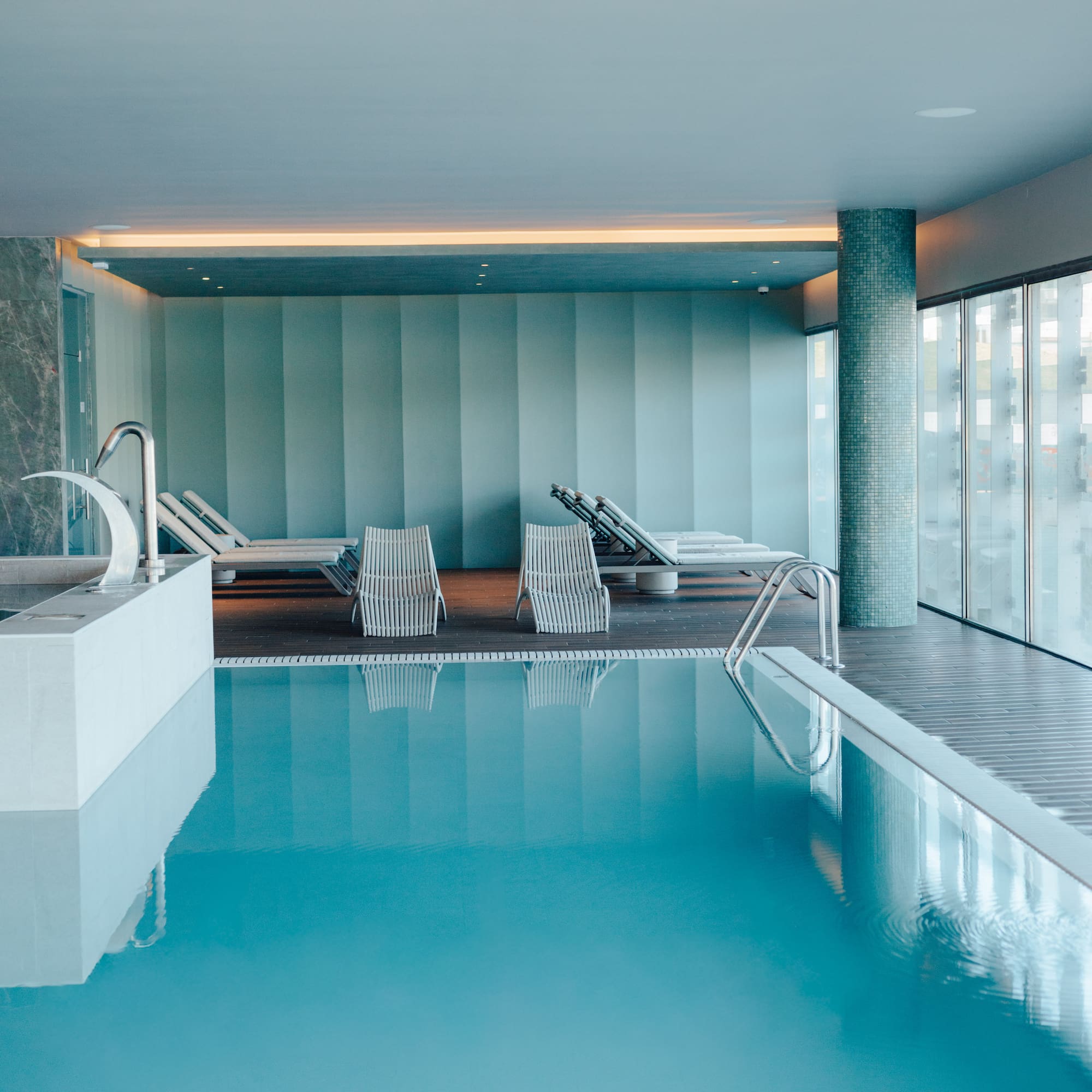 Indoor pool with sun loungers, blue water, modern spa design.