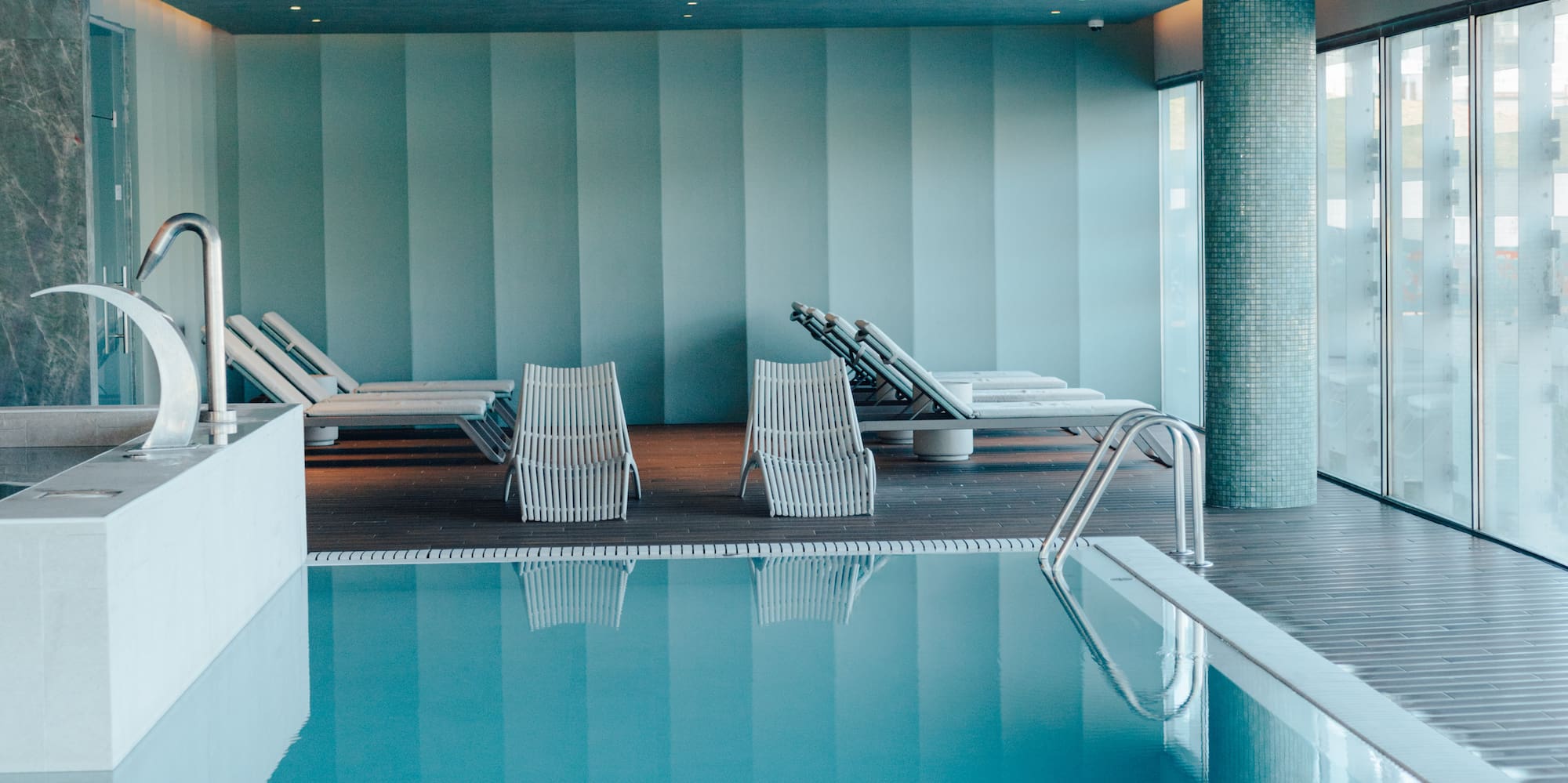 Indoor pool with sun loungers, blue water, modern spa design.