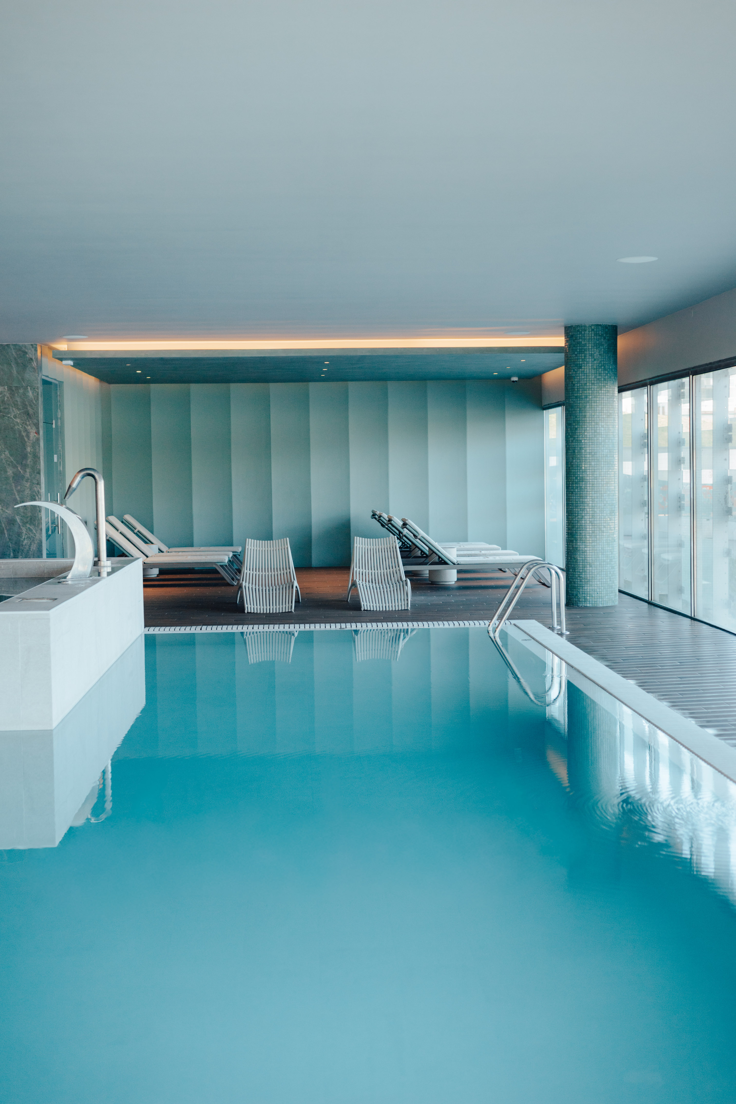Indoor pool with sun loungers, blue water, modern spa design.