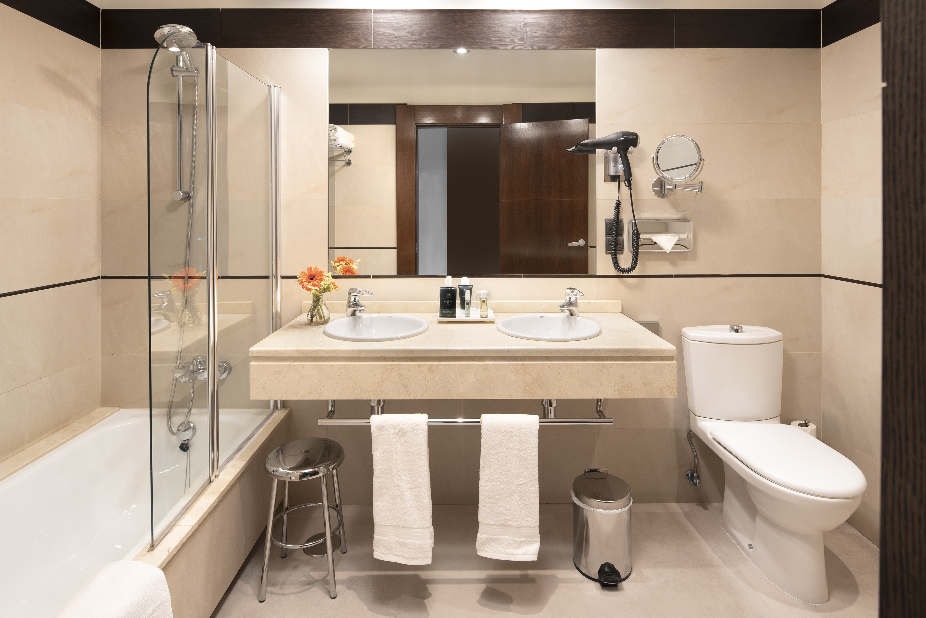 Modern beige bathroom with dual sinks, bathtub, shower, and toilet.