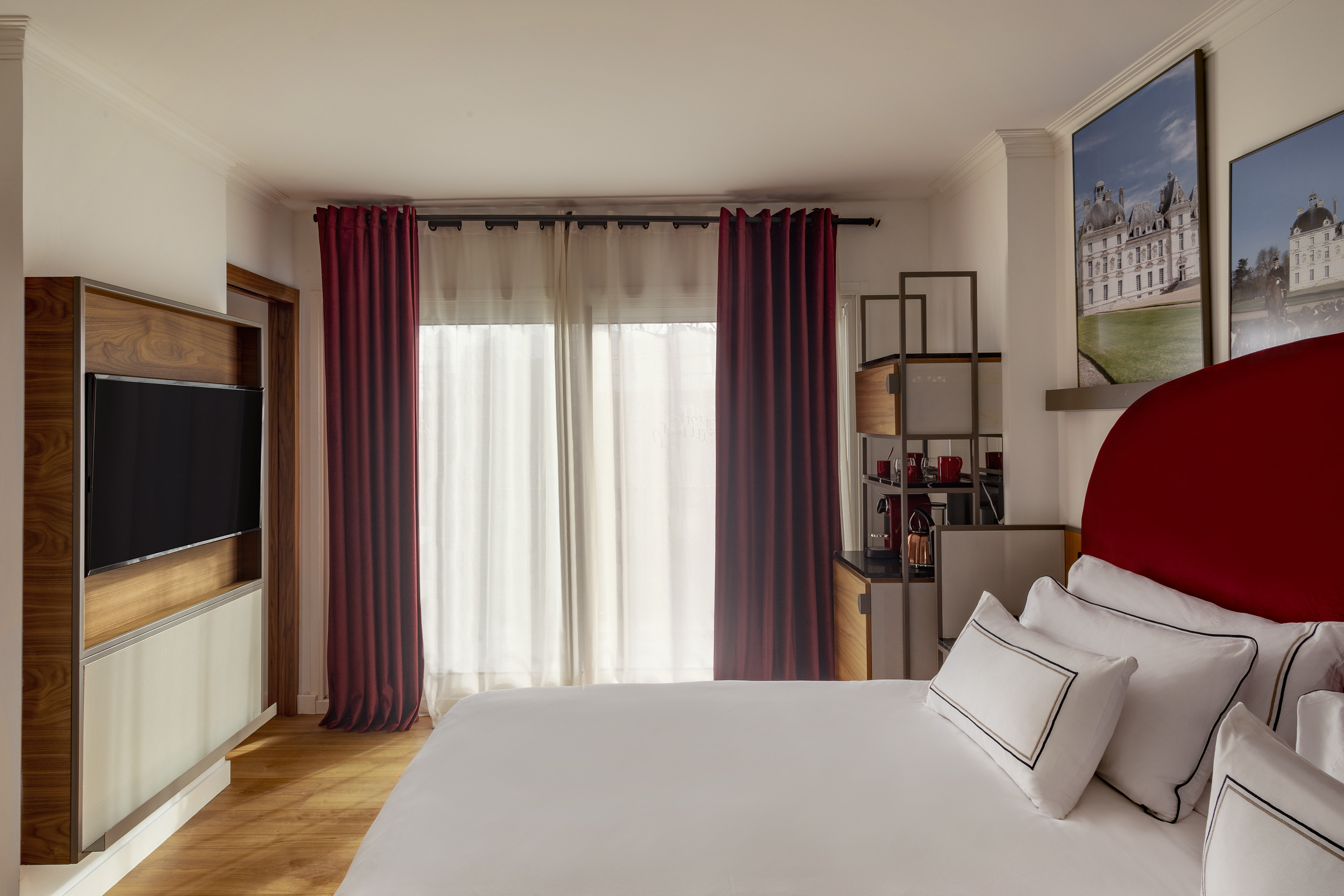 Modern hotel bedroom with white bed, red headboard, mounted TV, and red drapes.