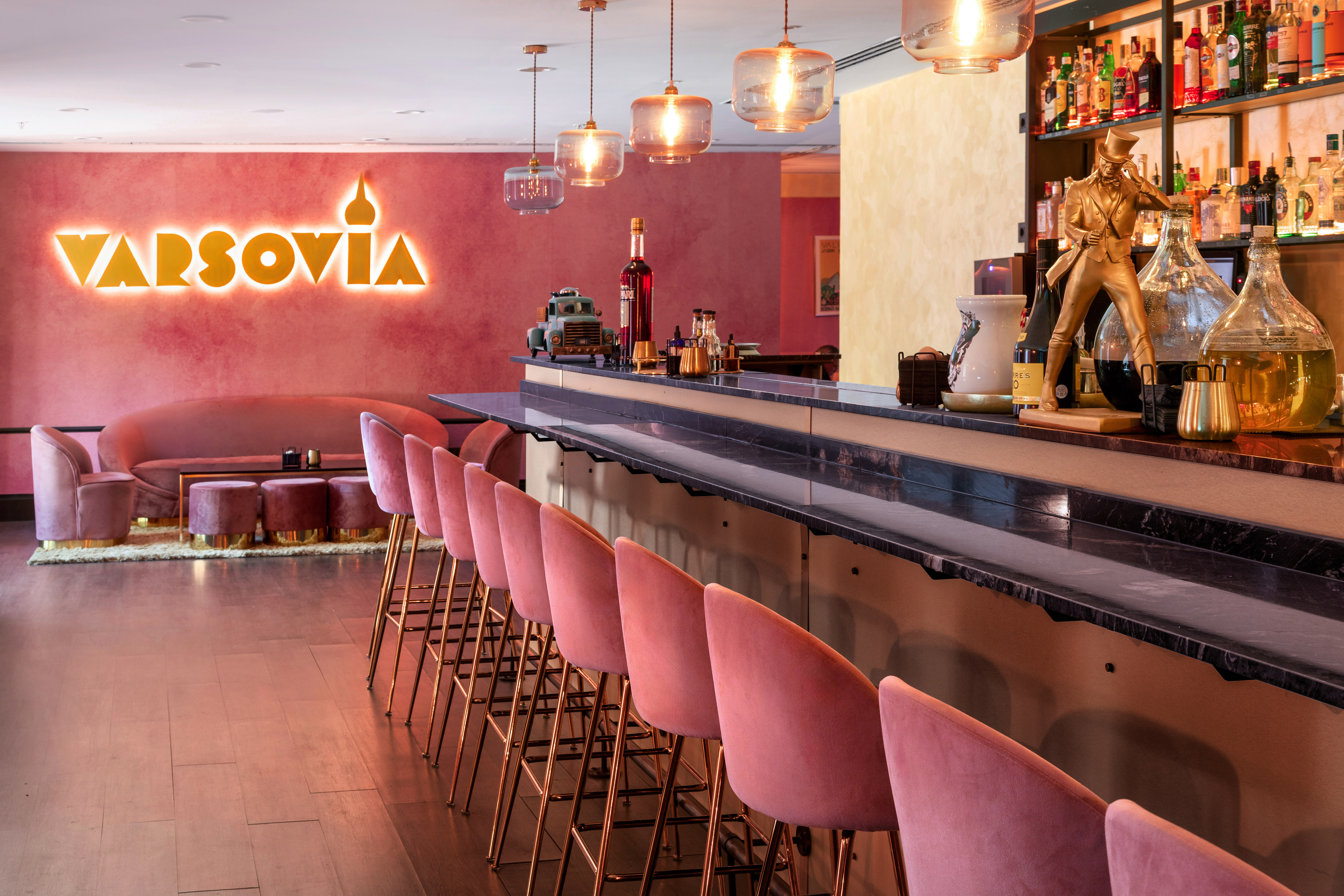 Stylish pink and gold bar interior with VARSOVIA neon sign and velvet stools.