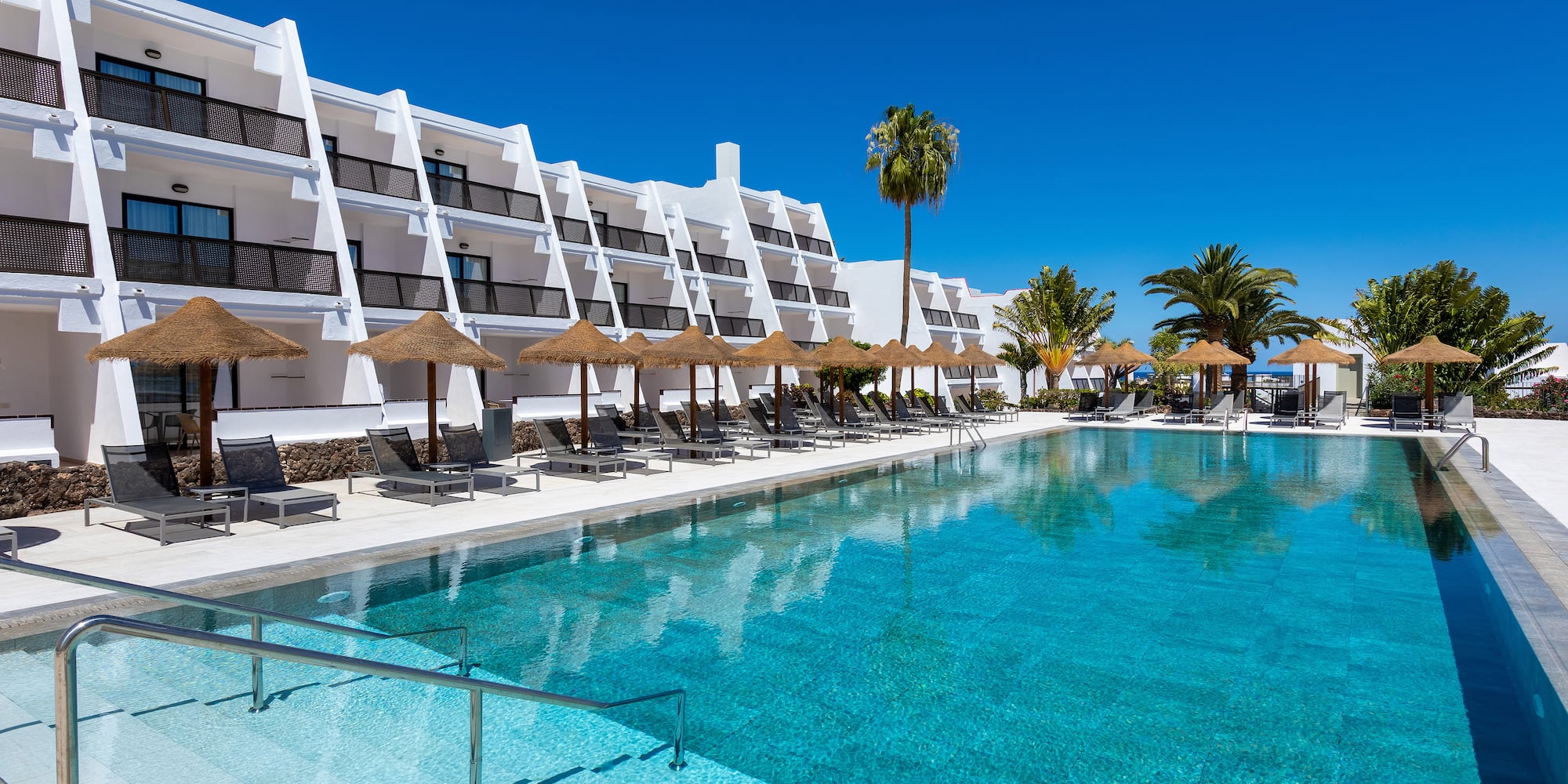 a pool with umbrellas and chairs in front of a building