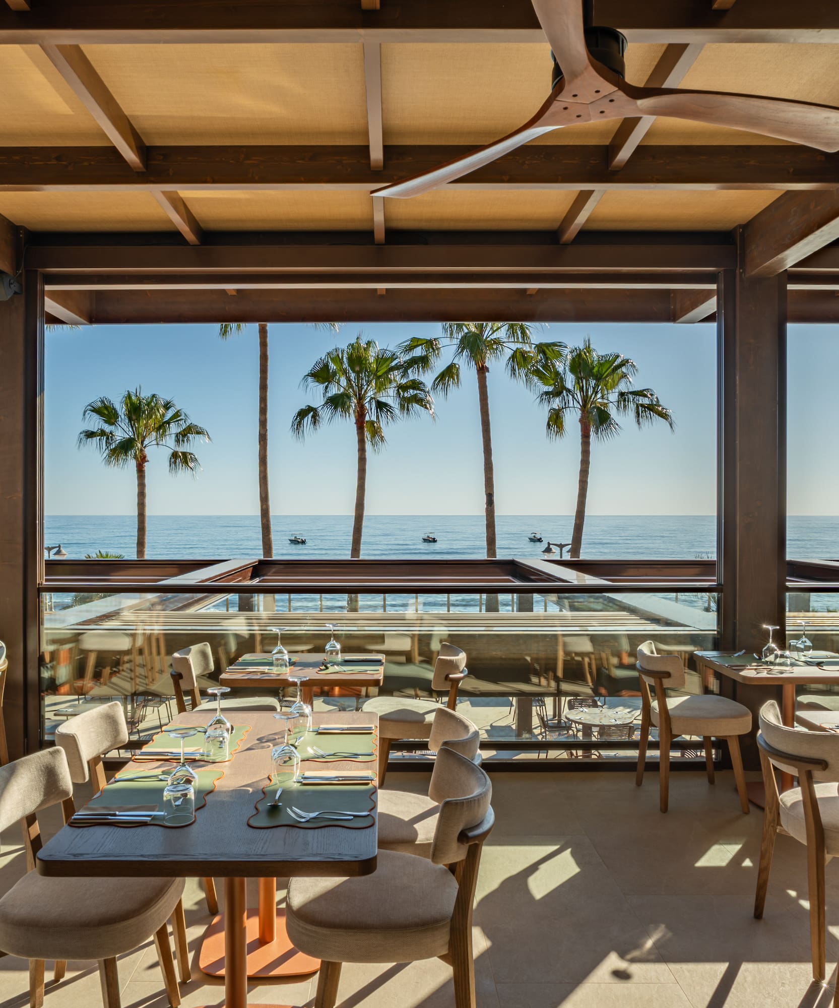 Scenic outdoor restaurant overlooking ocean, palm trees, and set tables.