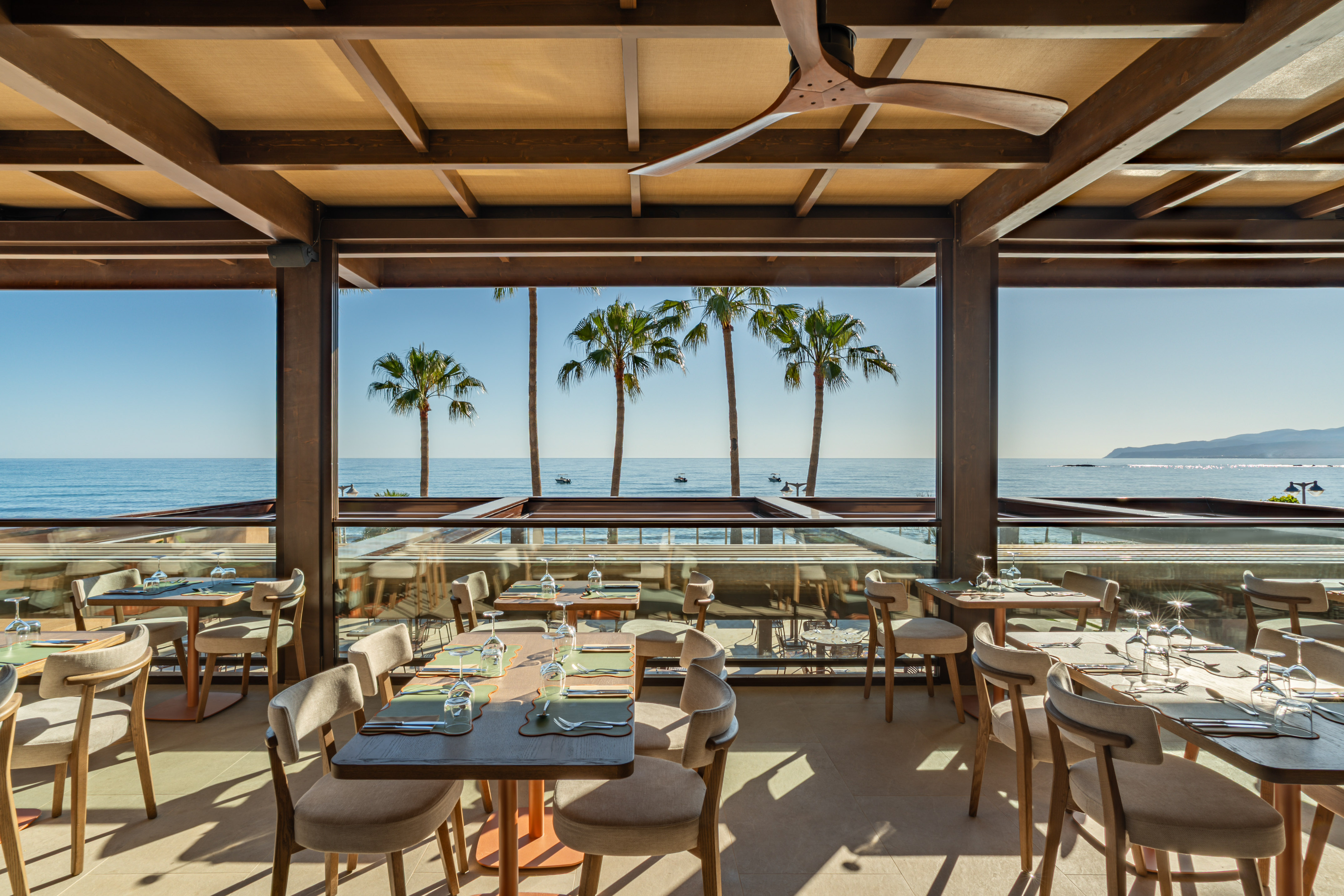 Scenic outdoor restaurant overlooking ocean, palm trees, and set tables.