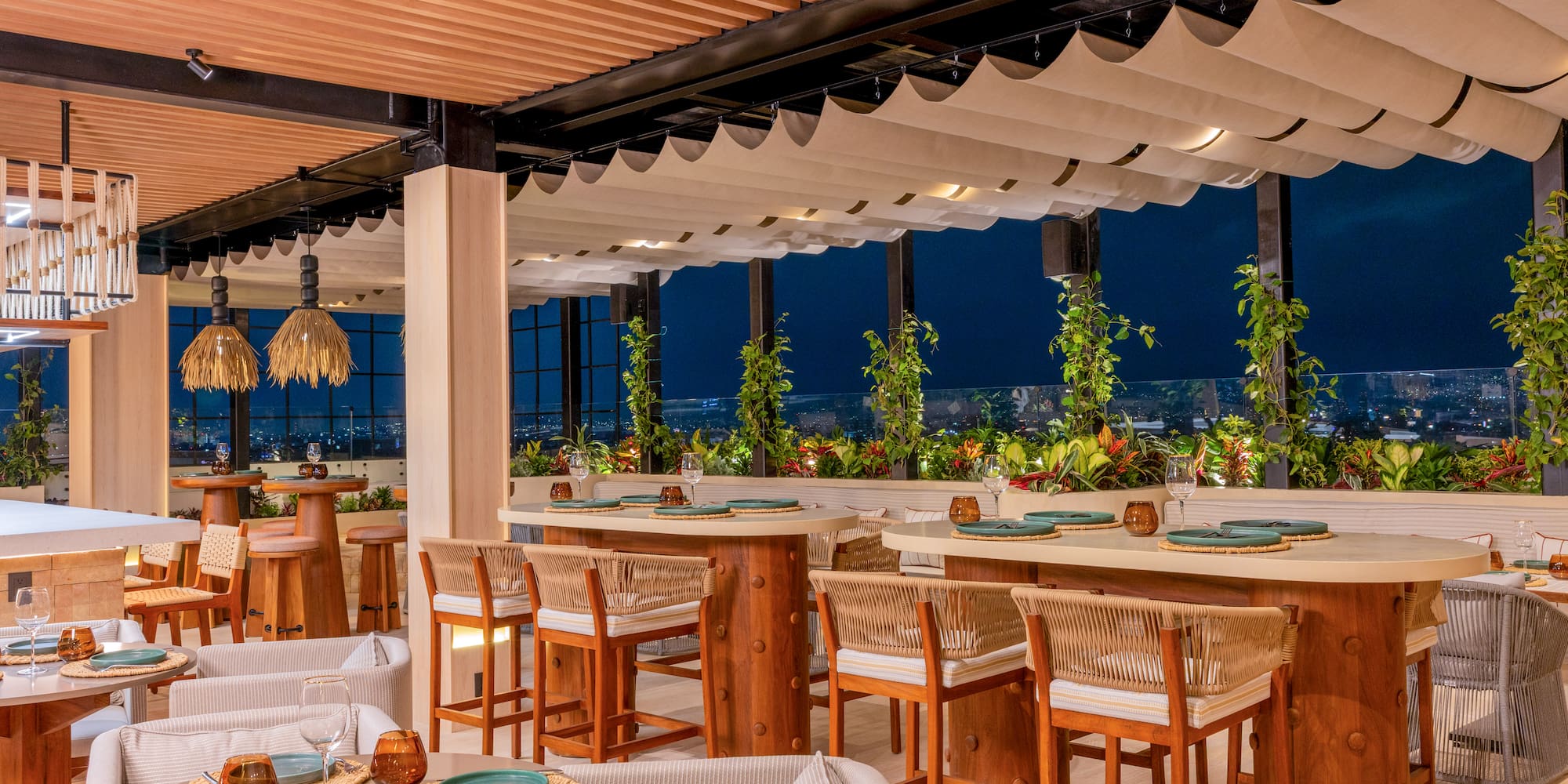 Modern rooftop restaurant, wooden tables, night city view, lush greenery.