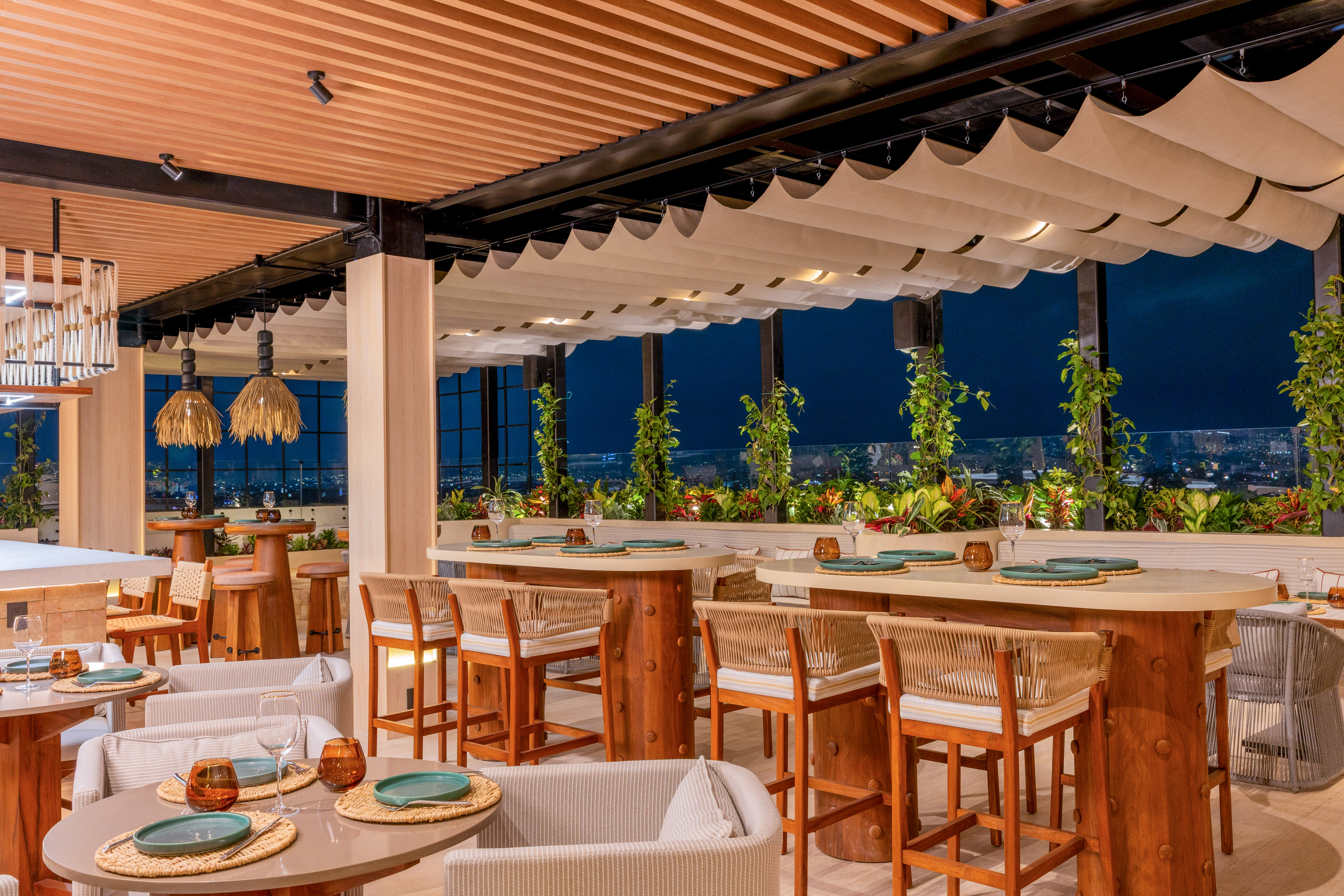 Modern rooftop restaurant, wooden tables, night city view, lush greenery.