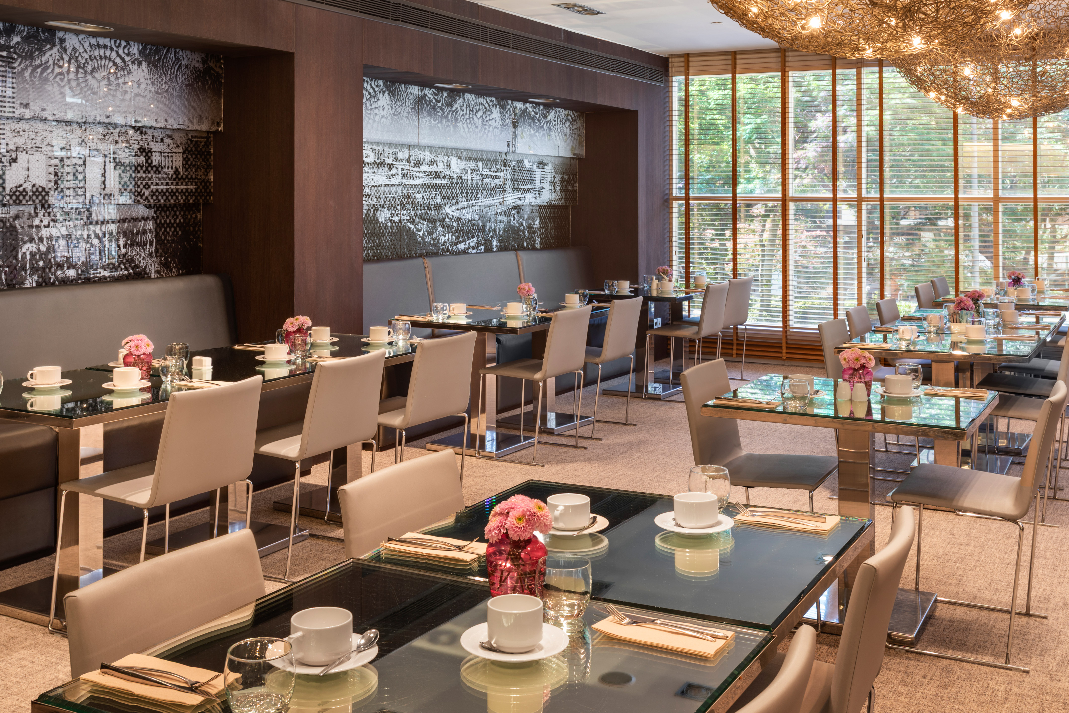 Modern restaurant dining room with glass tables, chairs, and cityscape wall art.