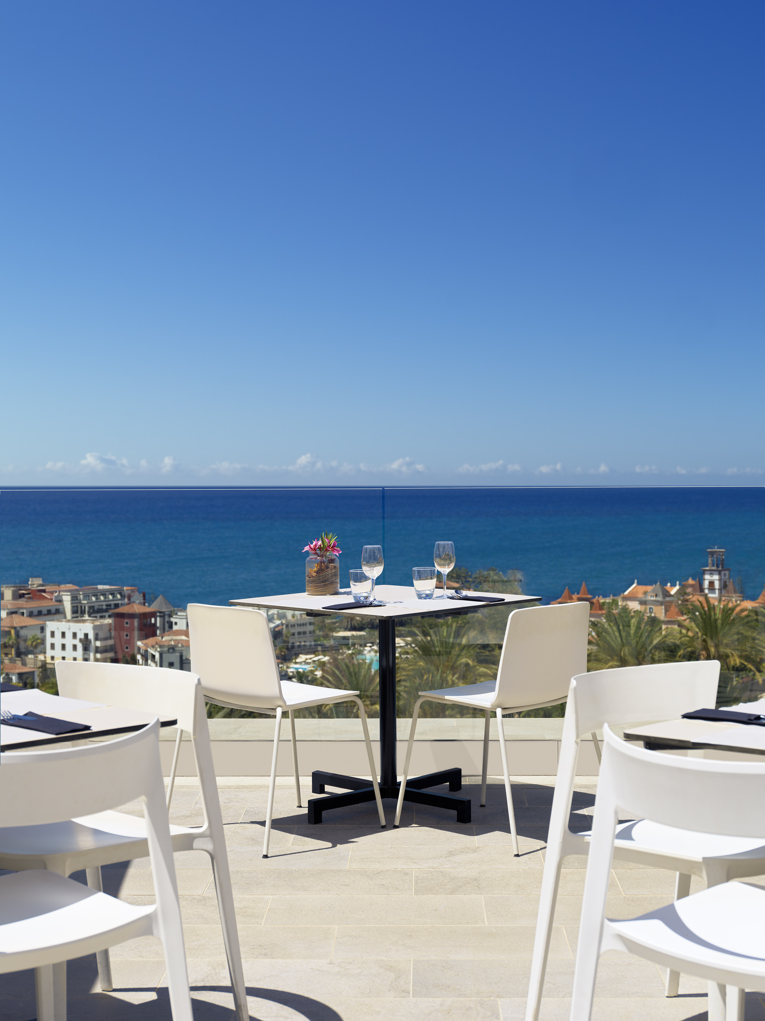 Ocean view dining table on a sunny terrace overlooking a coastal town.