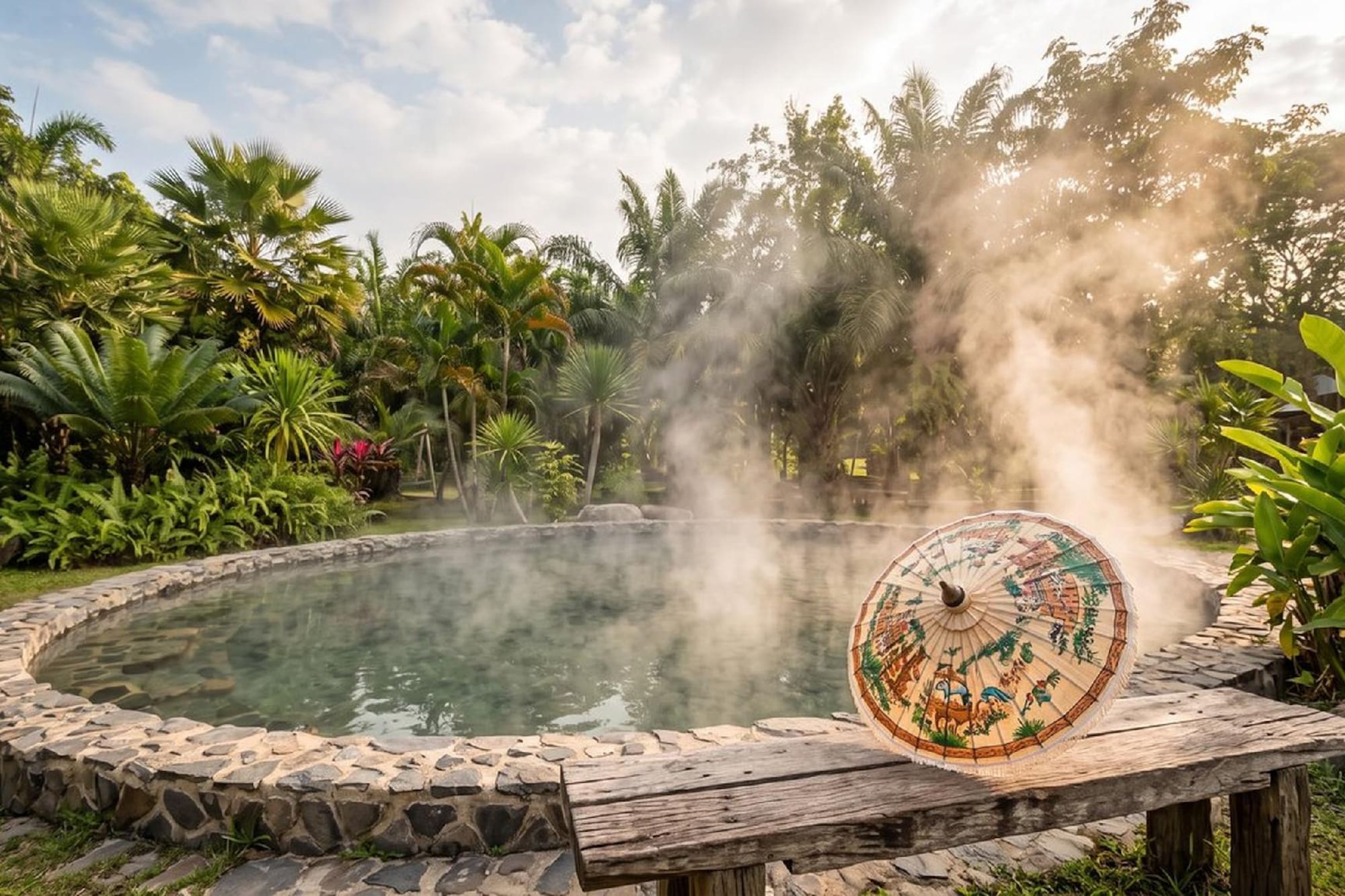 Tropical hot spring with steam, stone border, and decorative parasol.