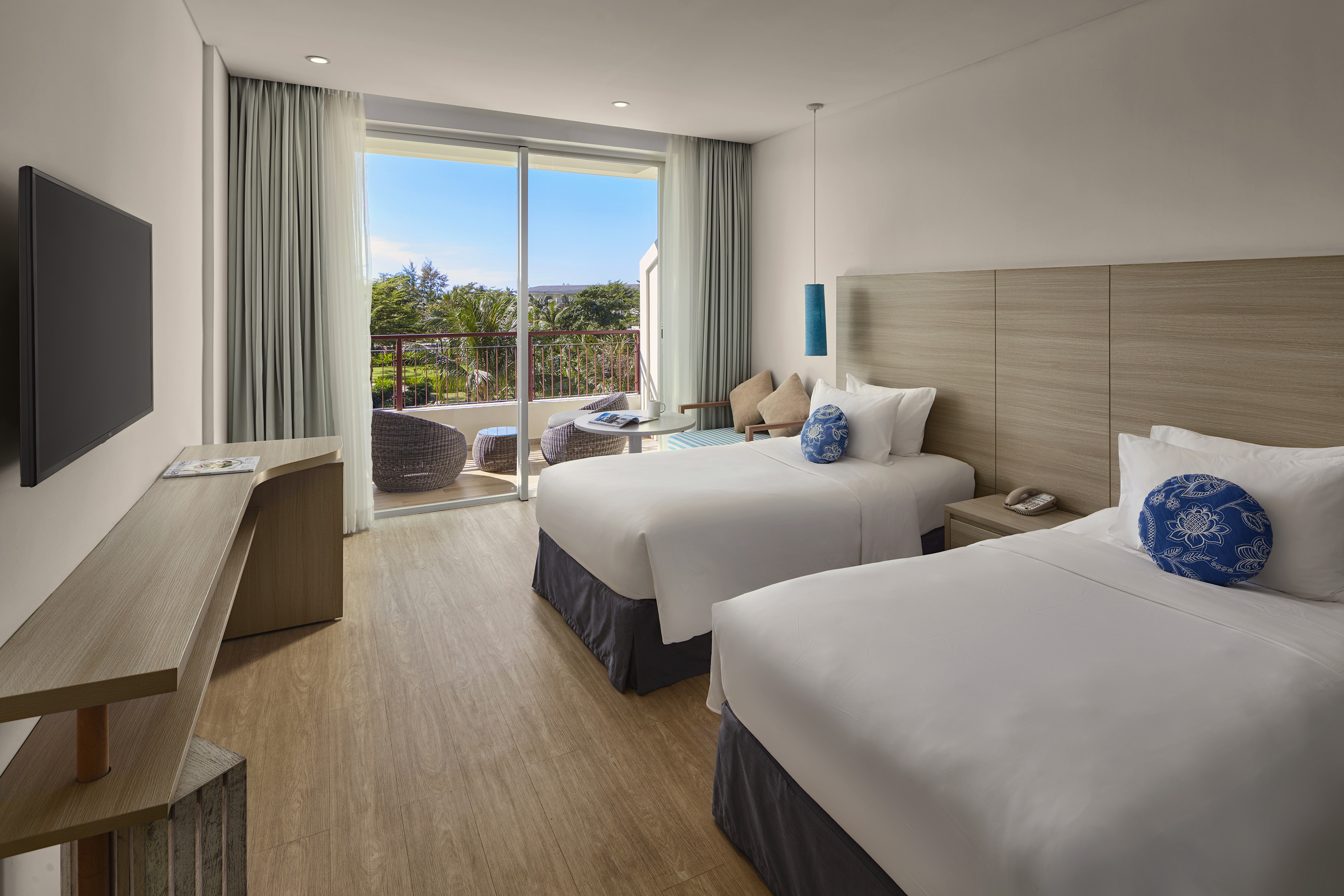 Bright hotel room with twin beds and a balcony offering tropical views.