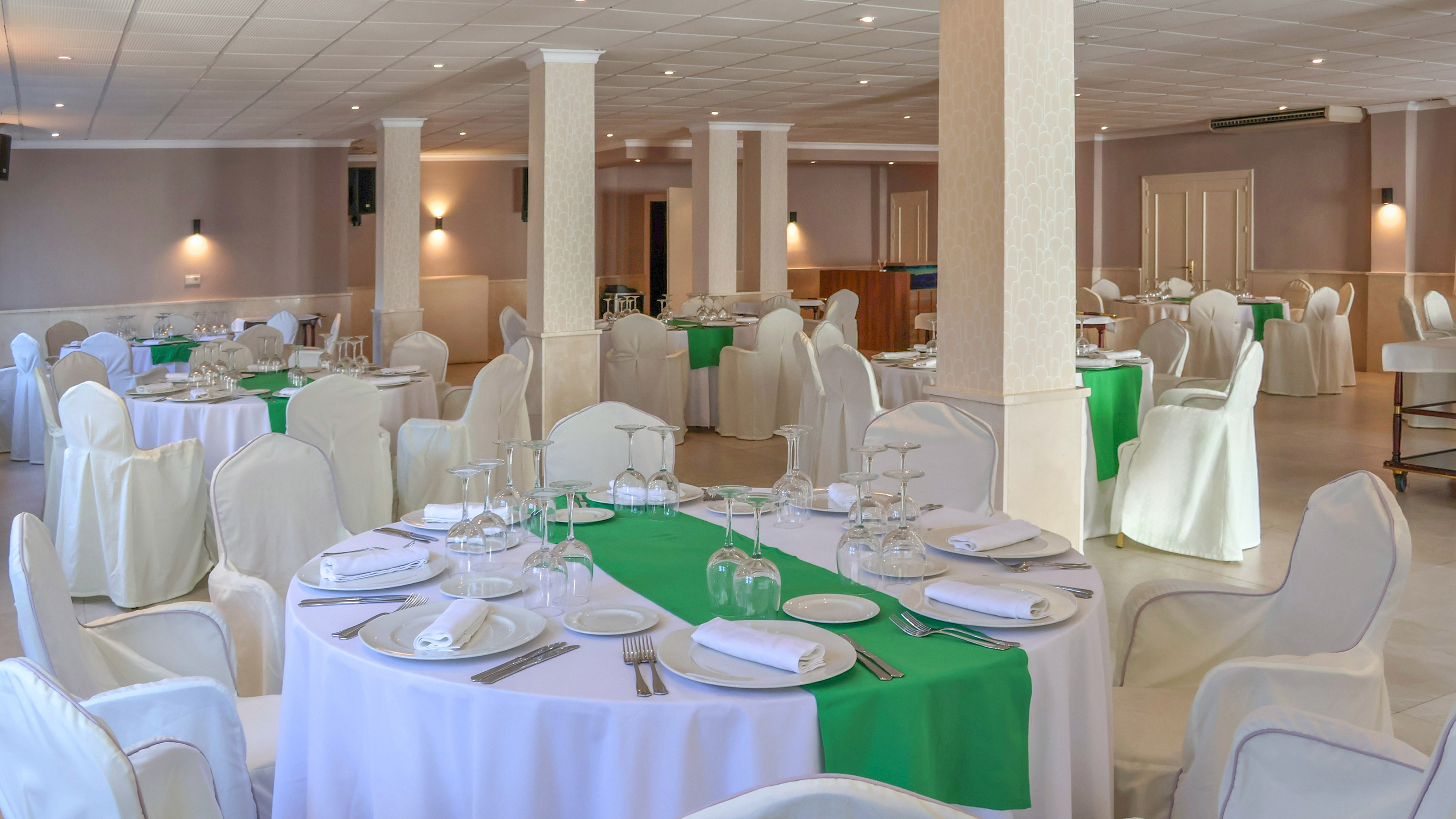 Banquet hall with white covered tables, green runners, and elegant place settings.