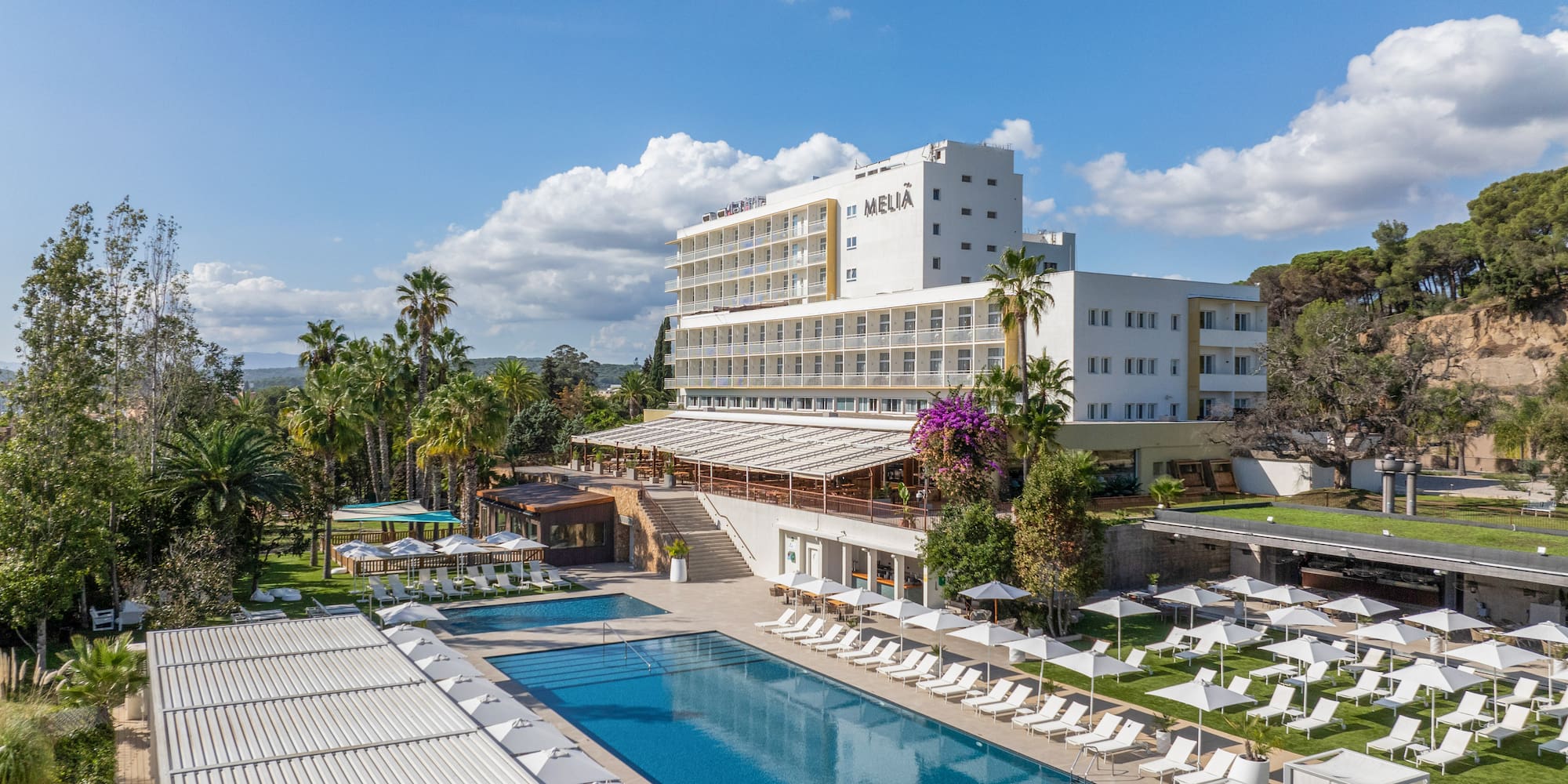 a pool with lounge chairs and a building with trees and blue sky