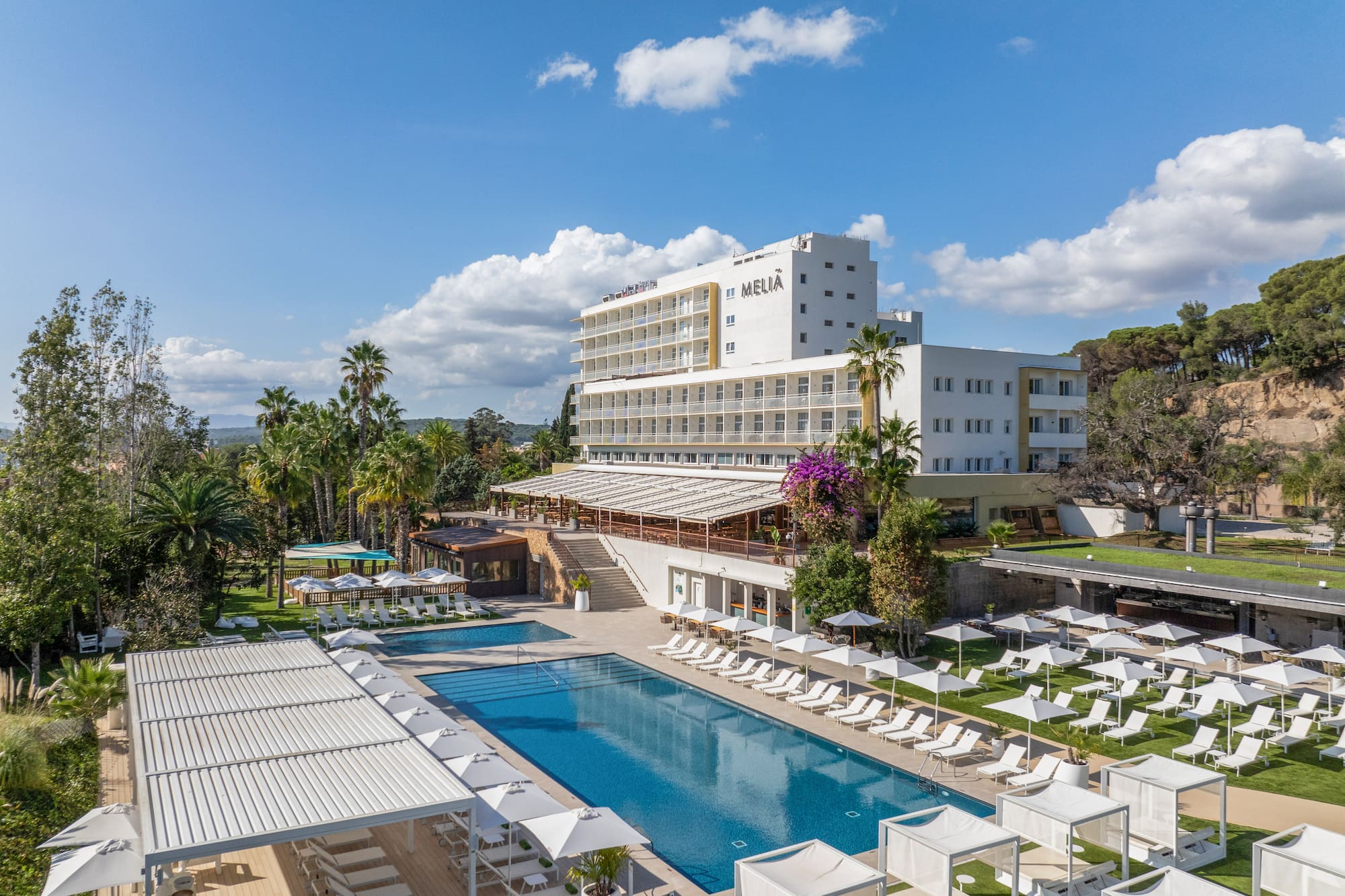 Aerial view: Meliá hotel, two pools, white loungers, and lush palm trees.