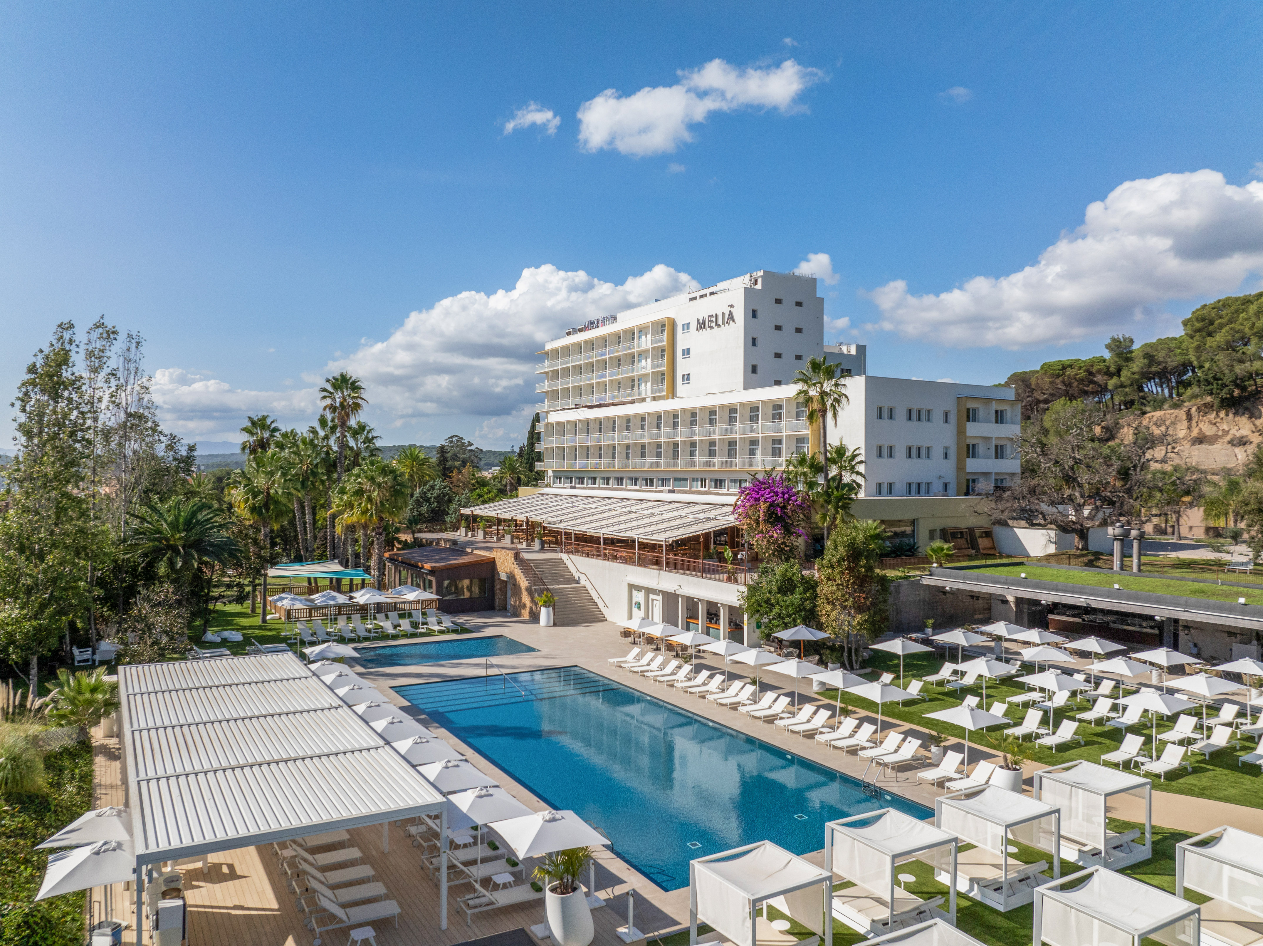 a pool with lounge chairs and a building with trees and blue sky