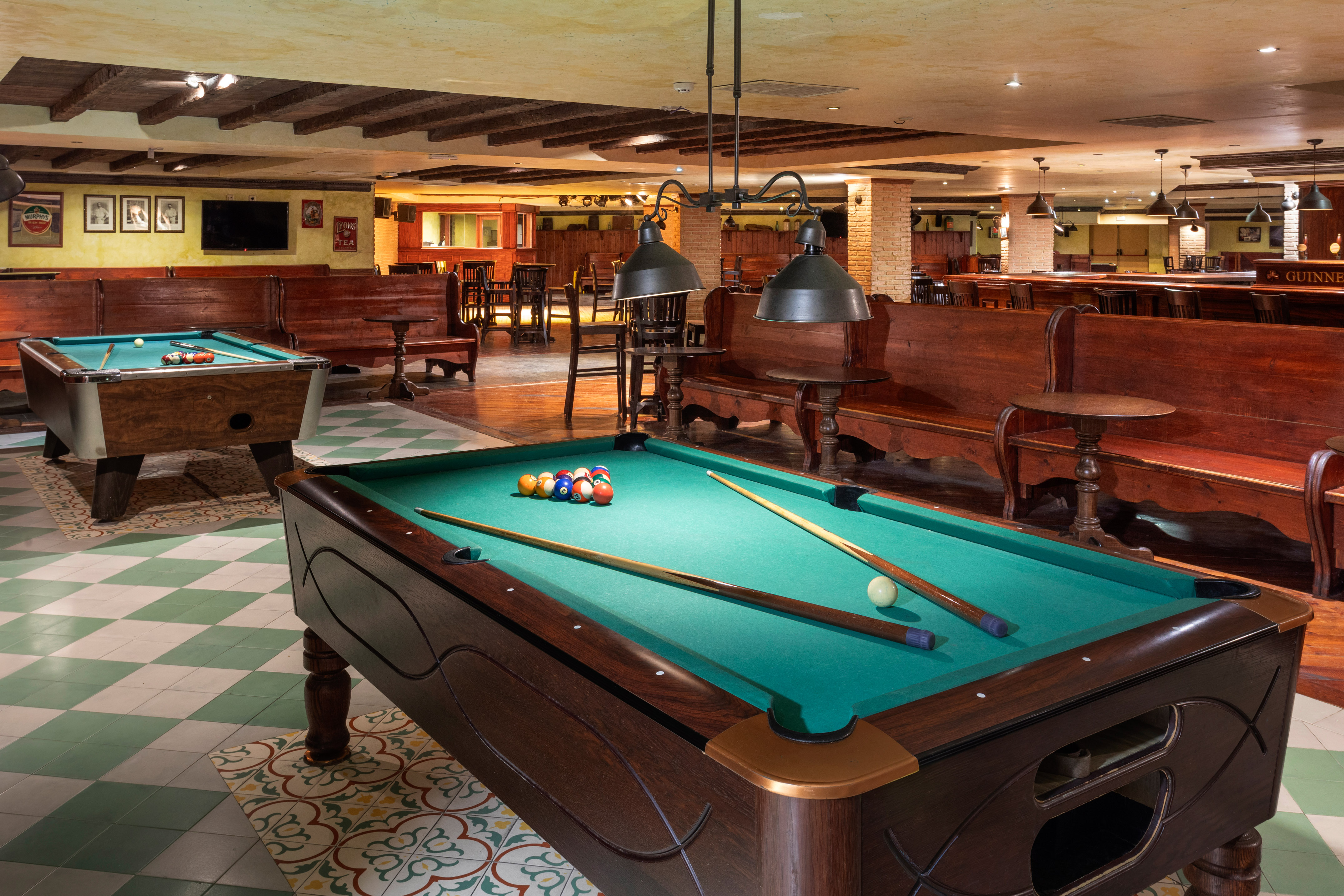 Classic pool hall with two billiard tables, wooden furniture, and warm lighting.